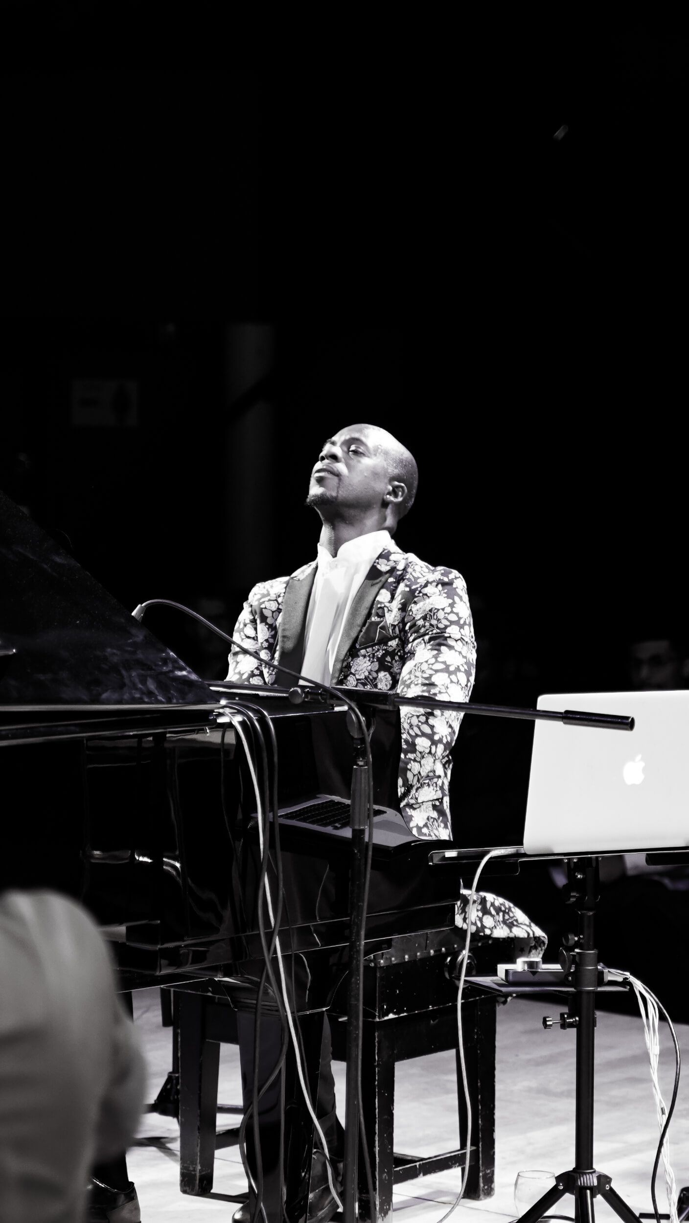 Pianist in floral suit performs on stage, eyes closed, under a spotlight. Black and white.