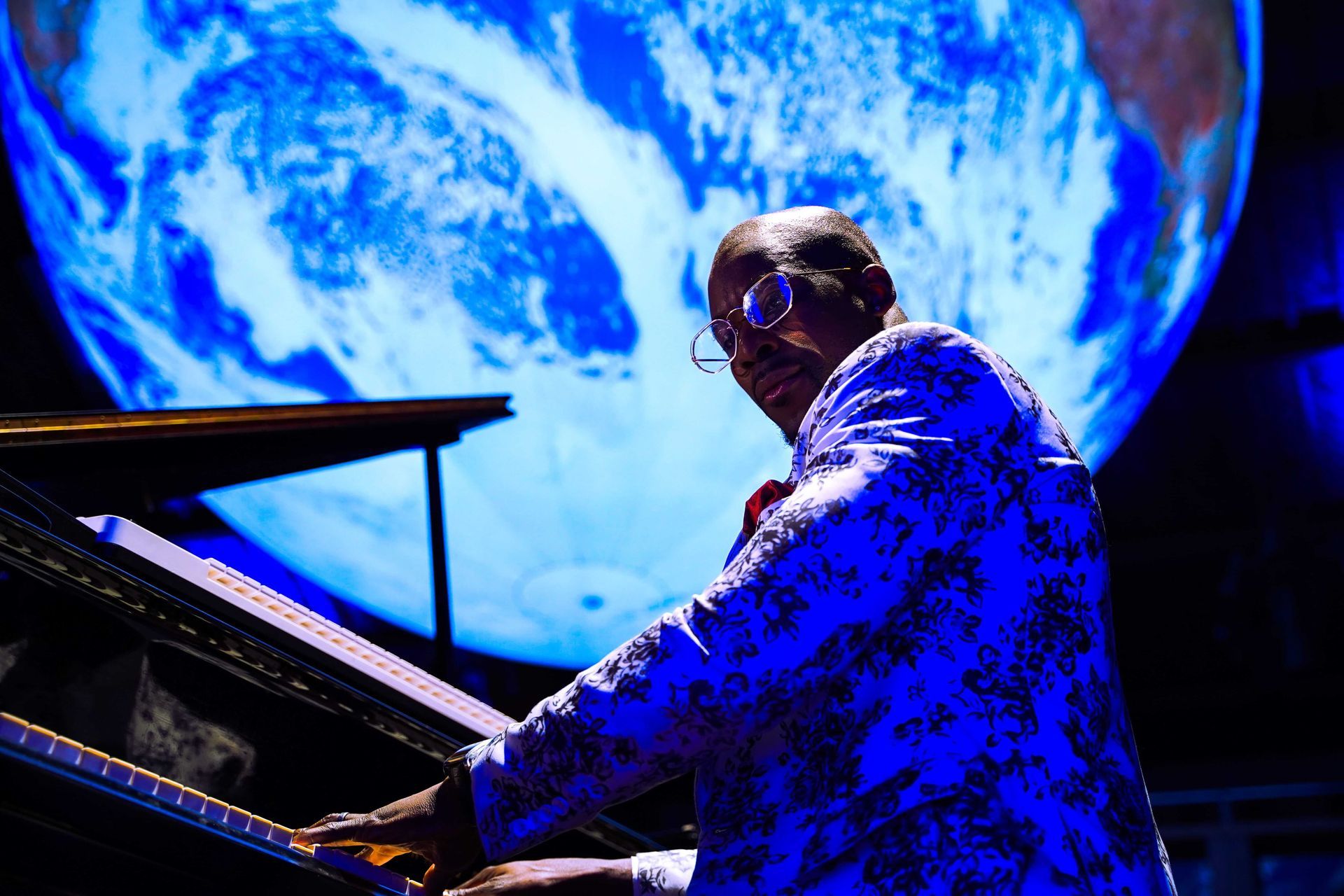 Pianist playing piano on stage with a blue, Earth-like backdrop.
