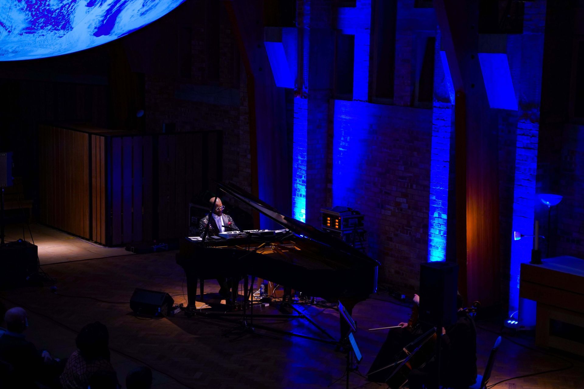 Pianist performing on stage, bathed in blue light. Piano and musician center, stage left, and audience in the shadows.
