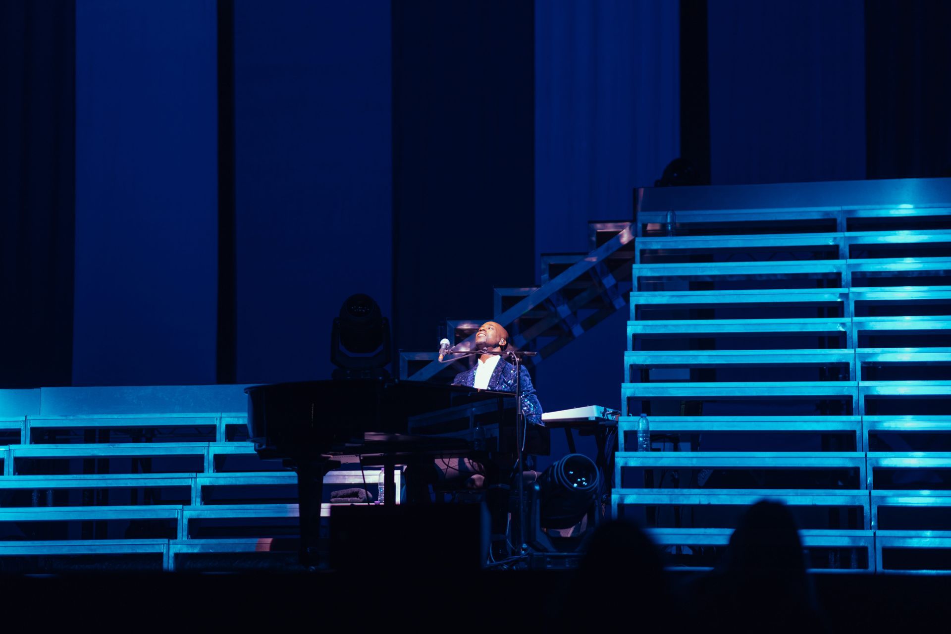 Man playing piano on a stage with blue lighting and stairs.