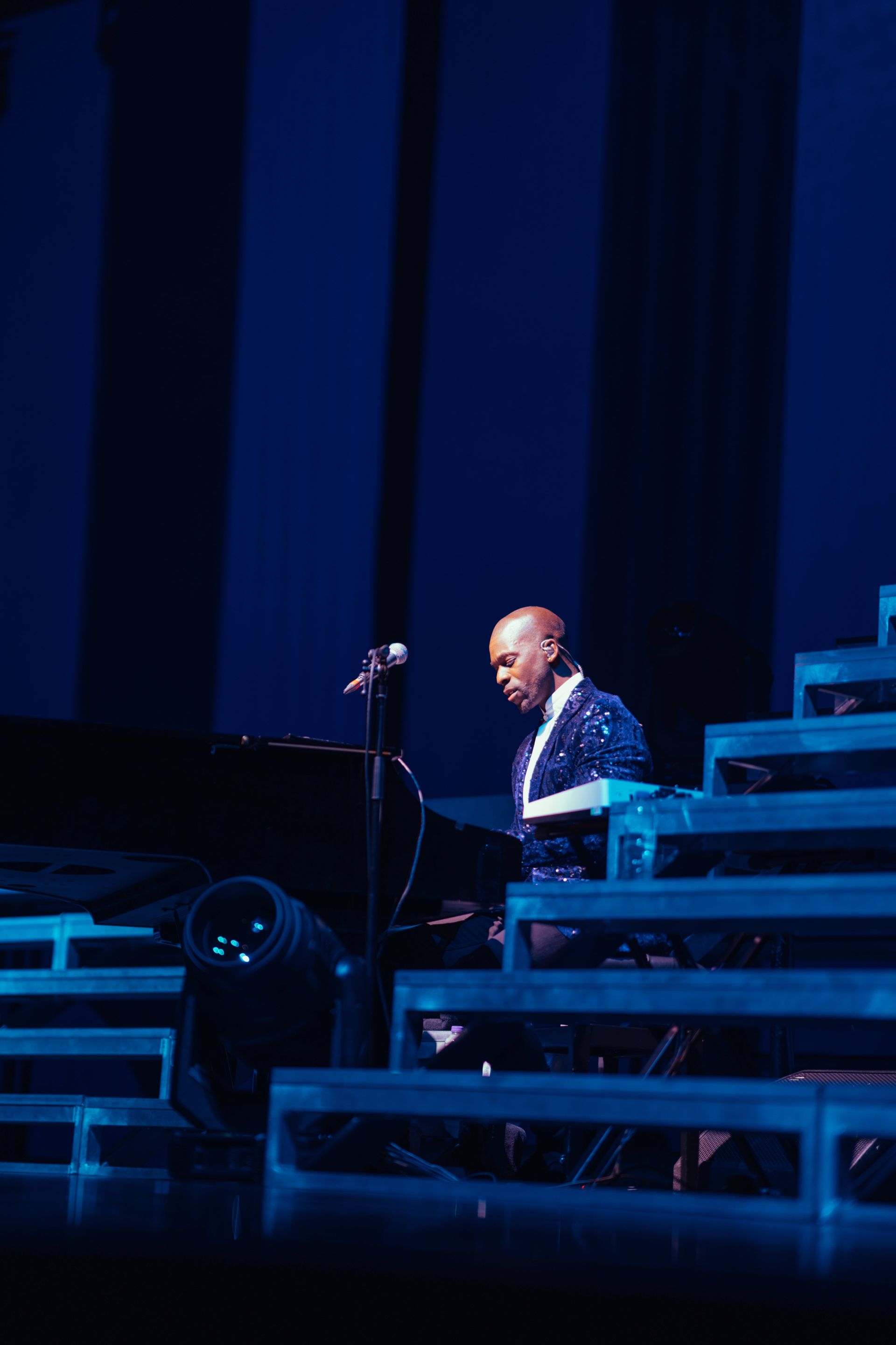 Pianist playing a grand piano on a stage with blue lighting.