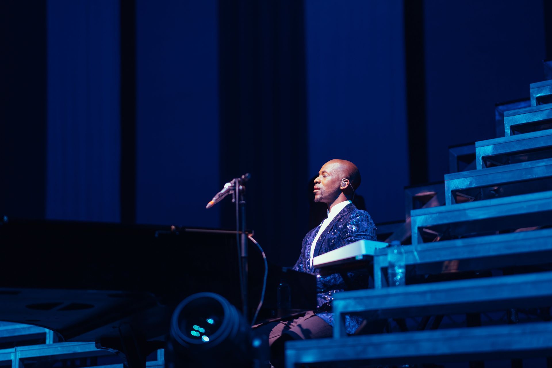 Person playing piano on stage, lit with blue light.
