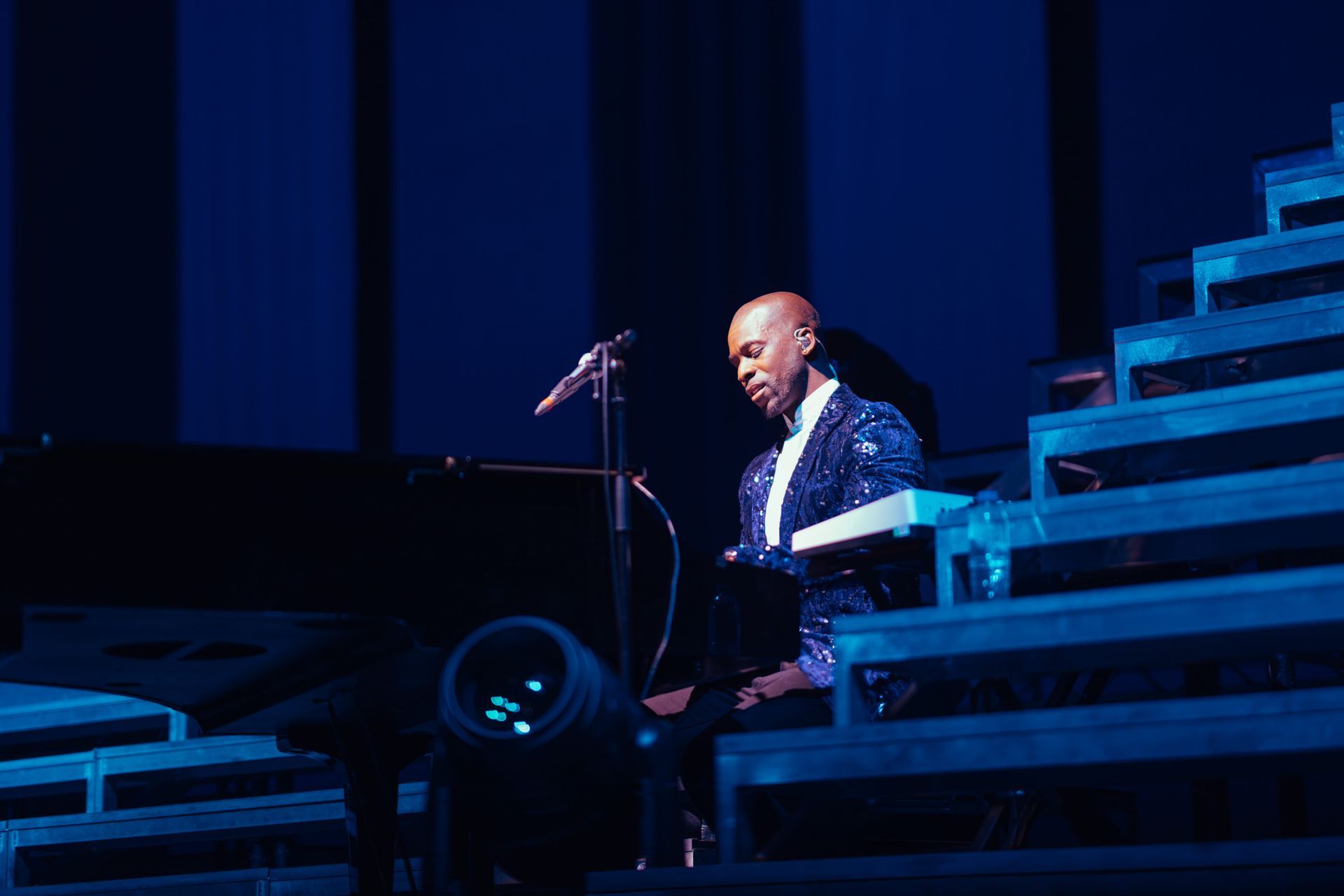 Man playing a keyboard on stage, illuminated by blue light.