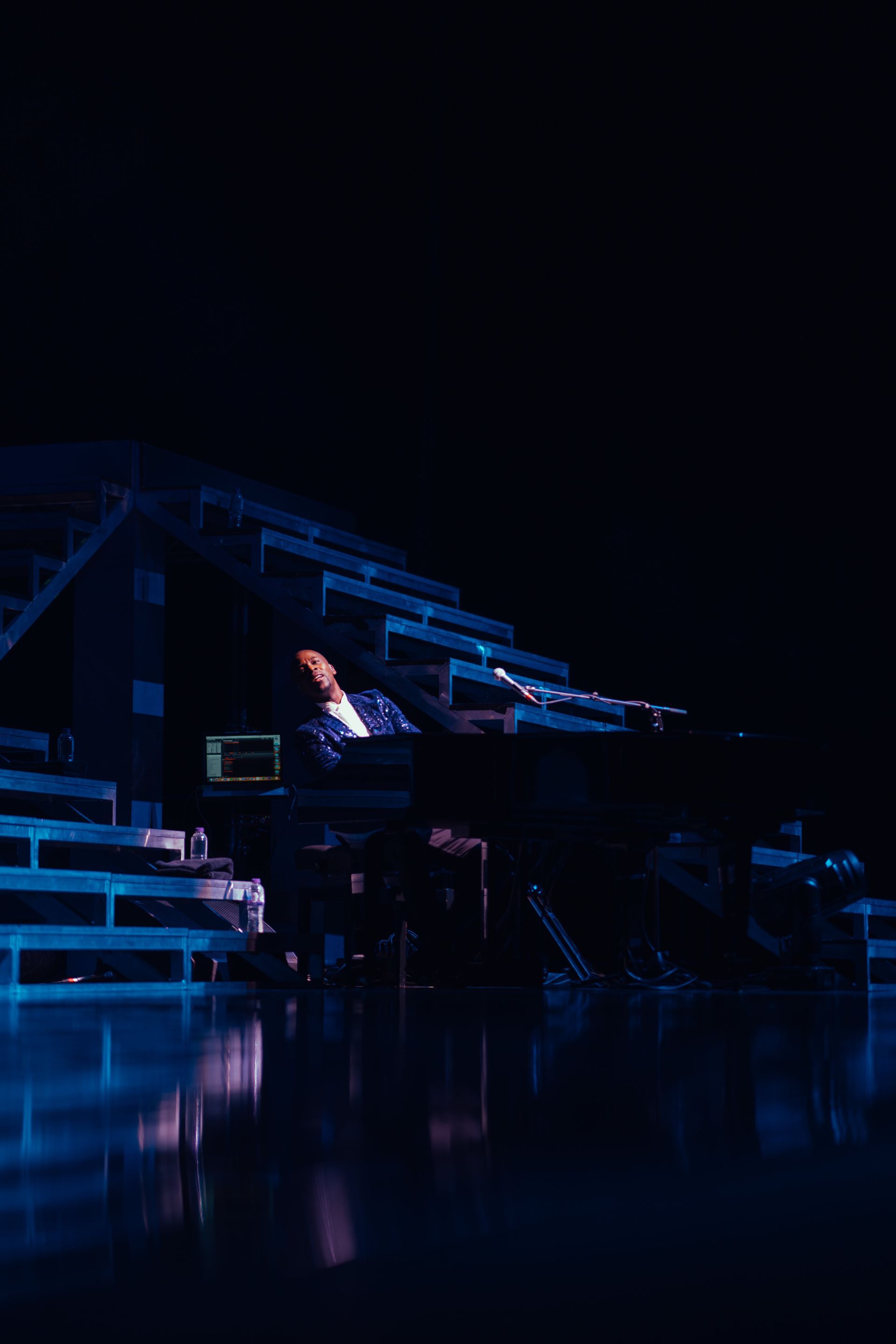 Person seated at a keyboard on a stage, dark setting with blue lighting.