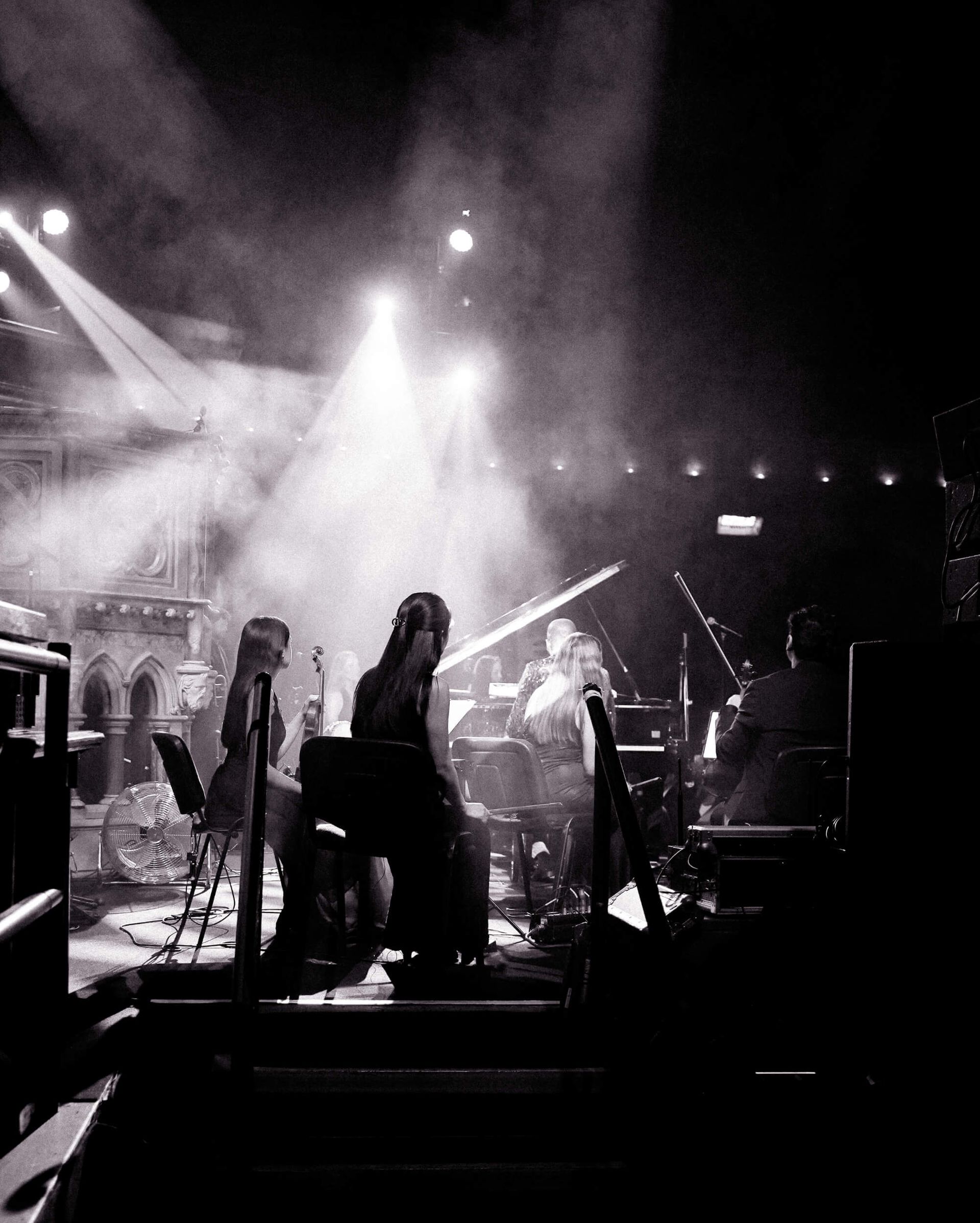 Band performing on stage, bathed in bright spotlights and smoky haze.