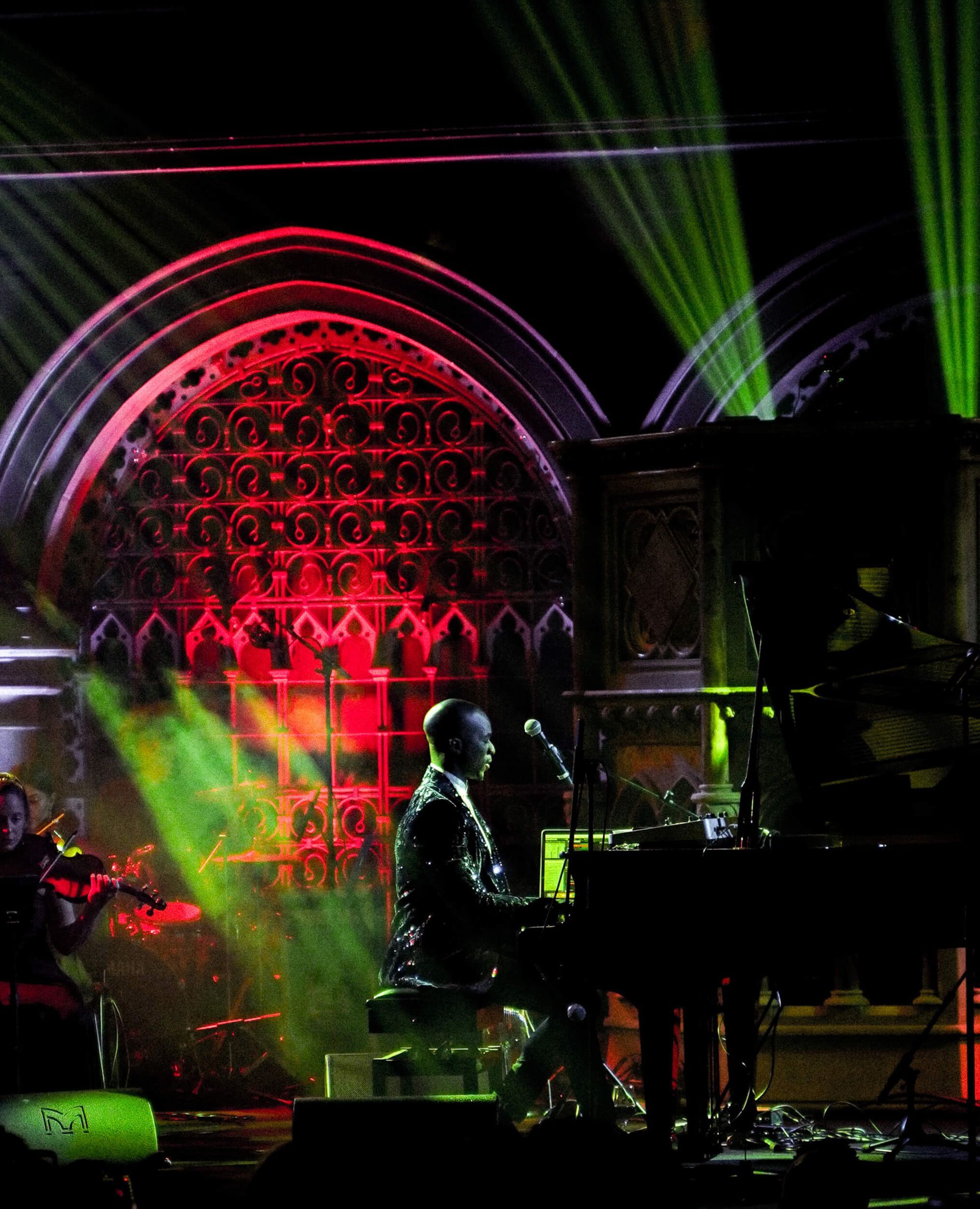 Man at piano performs on stage with red and green stage lights.