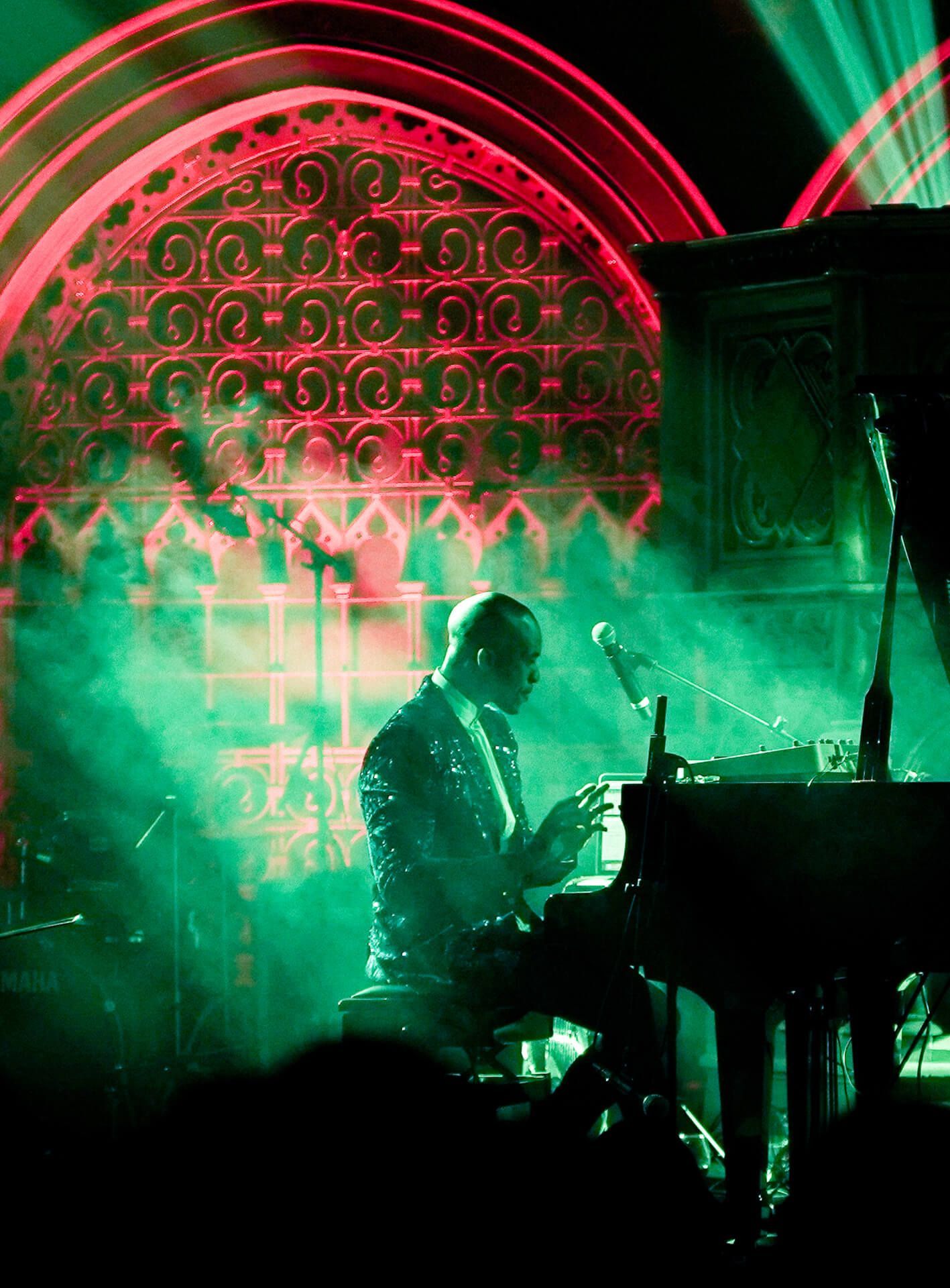 Pianist playing a grand piano on stage, bathed in green and red stage lights.
