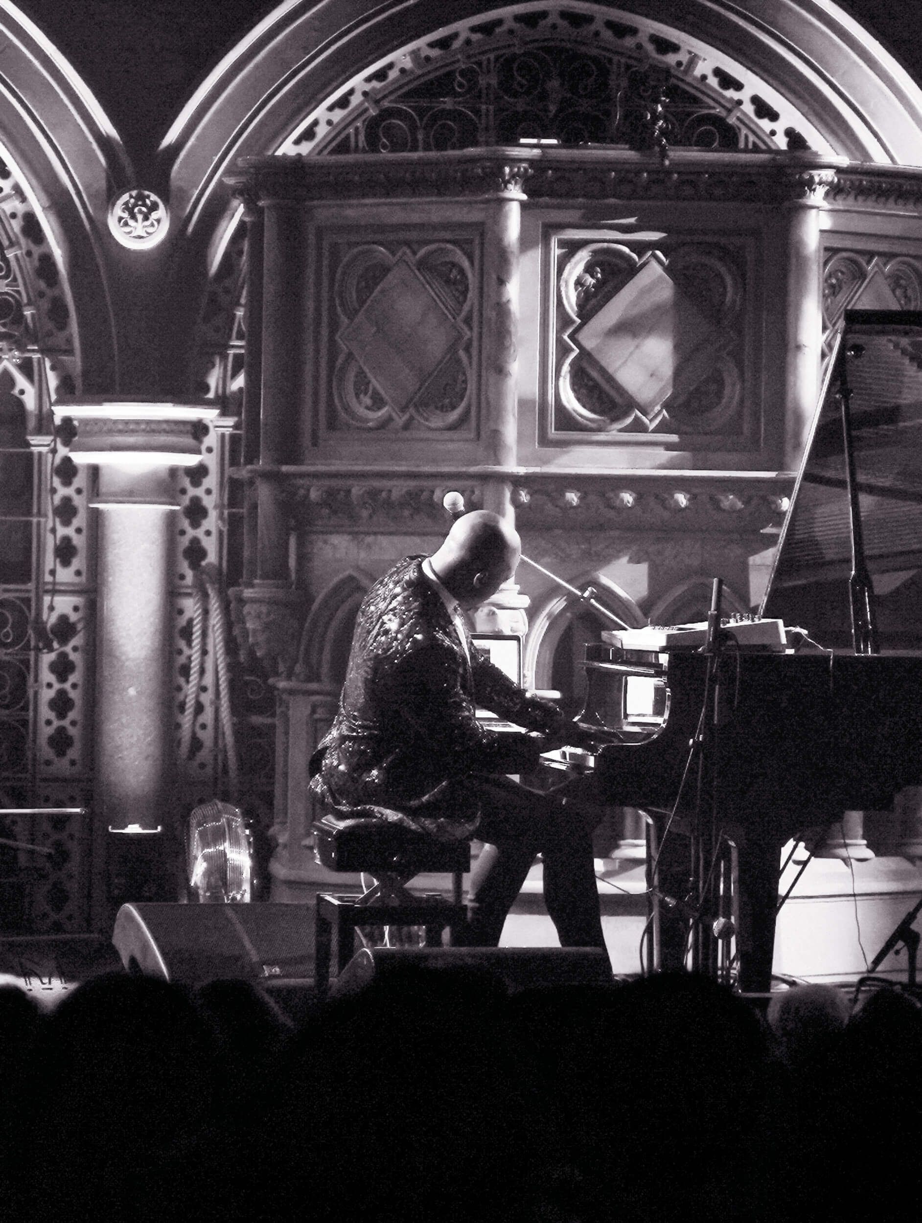 Pianist in a sparkly jacket performing in front of a decorative gothic-style backdrop.
