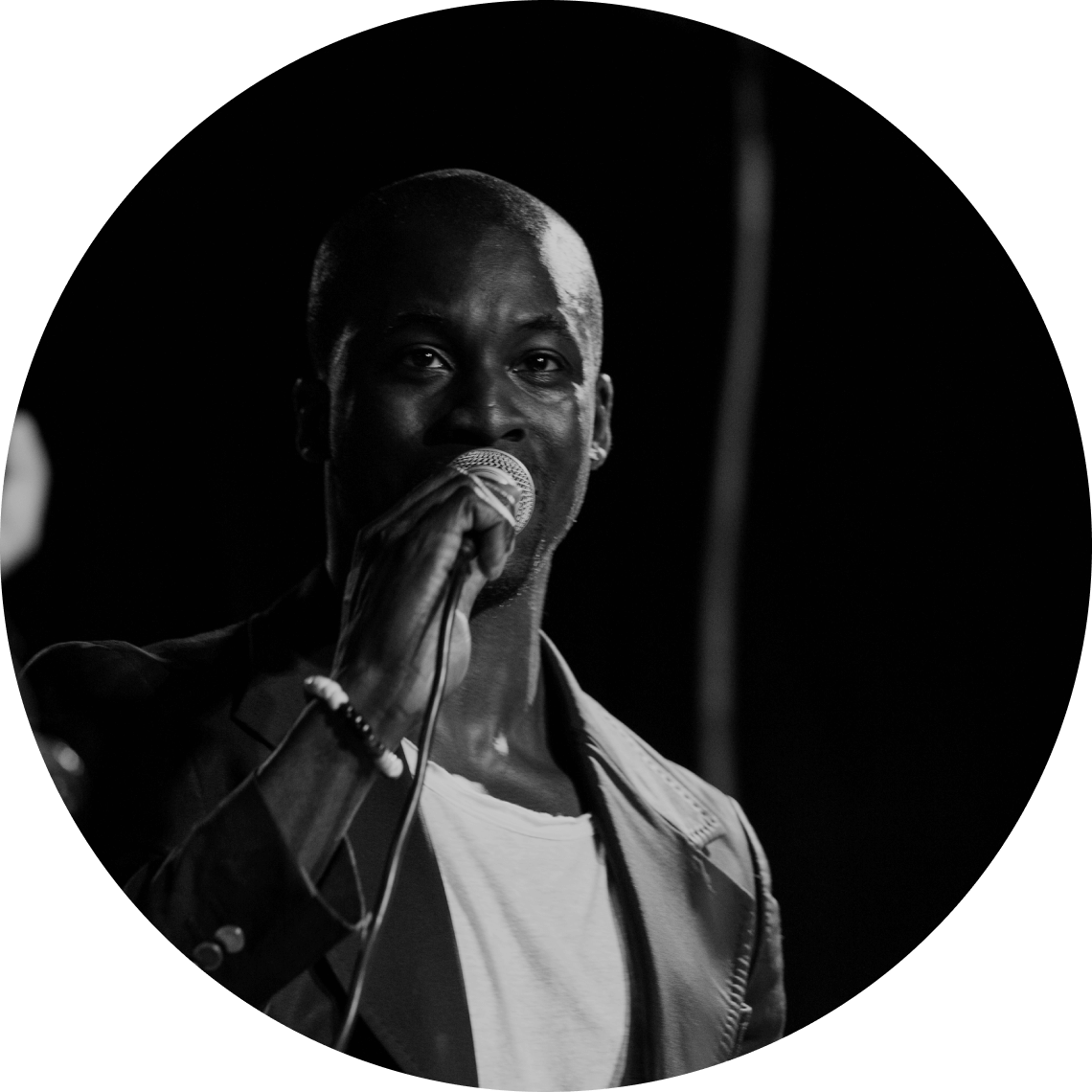 Man singing into a microphone on stage, black and white photograph.