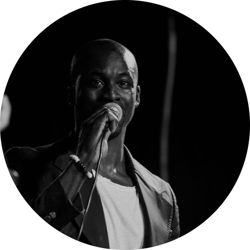 Man singing into a microphone on stage, black and white photograph.