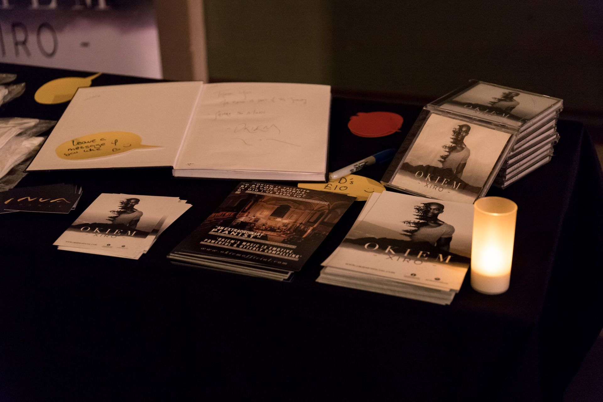 A table display with books and pamphlets, a lit candle, and a notebook in a dim setting.