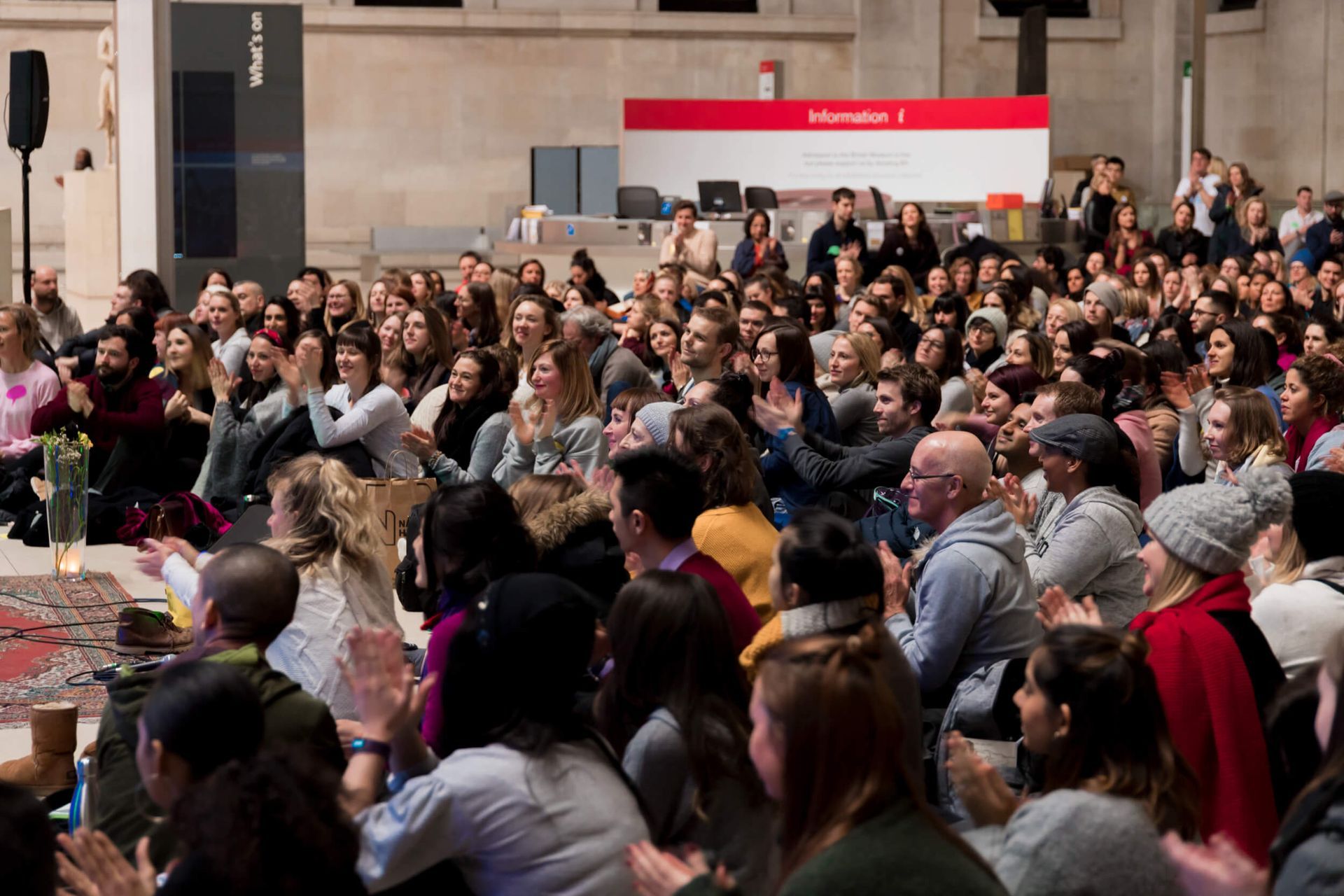 Large crowd clapping in an auditorium; red banner in the background.