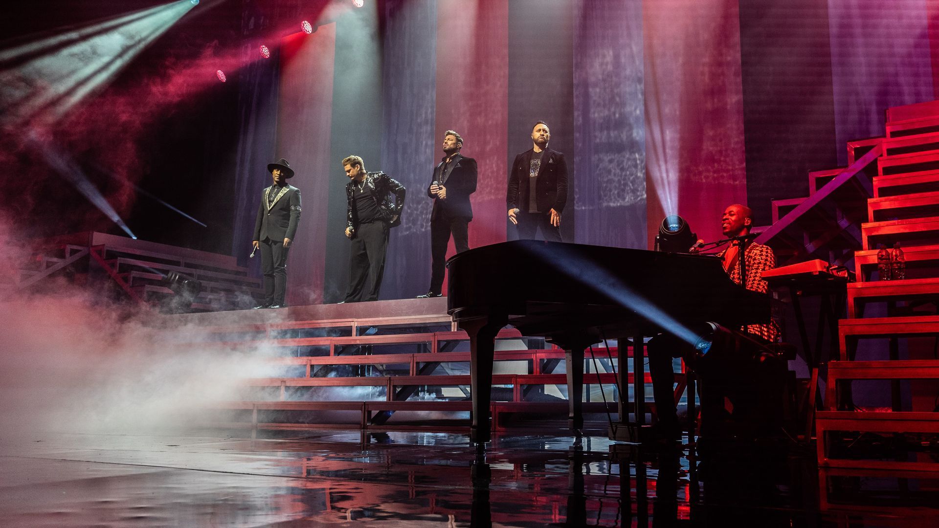 A musical group on a stage, performing with a piano and dramatic lighting.