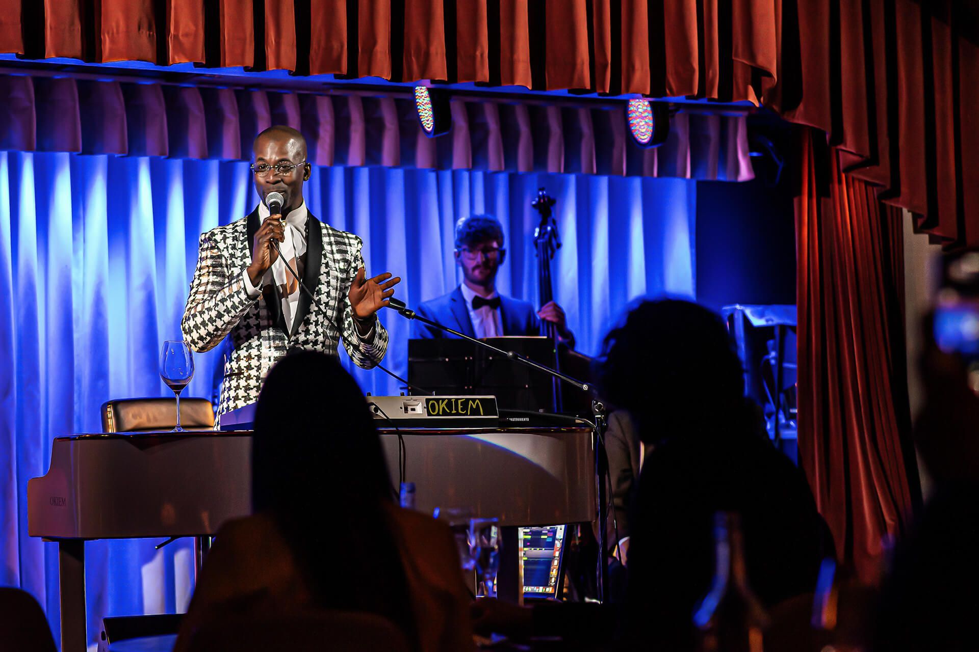Man in checkered suit singing with band at a club, audience in foreground.