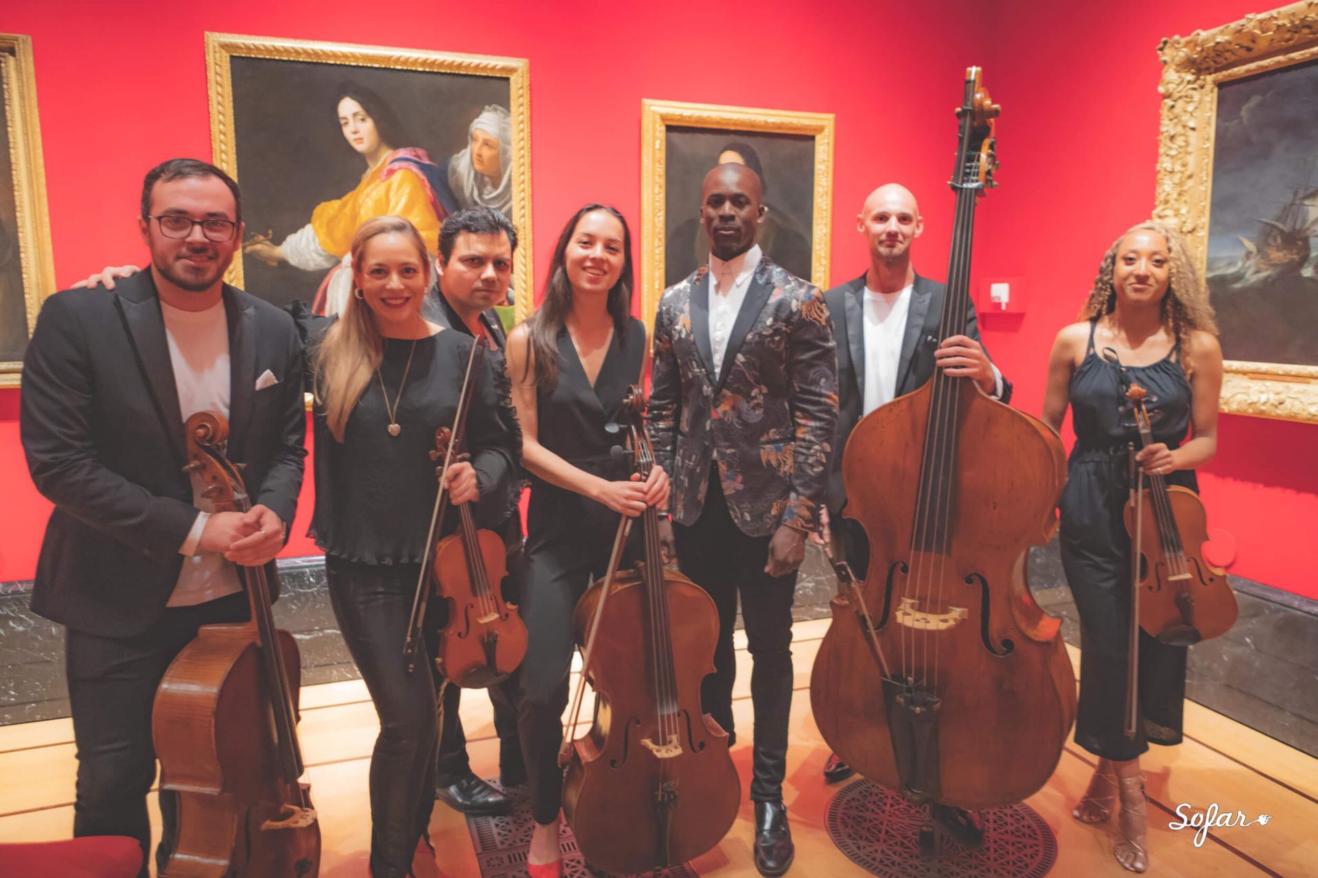 String ensemble, posing in art gallery with portraits on red walls; instruments held.