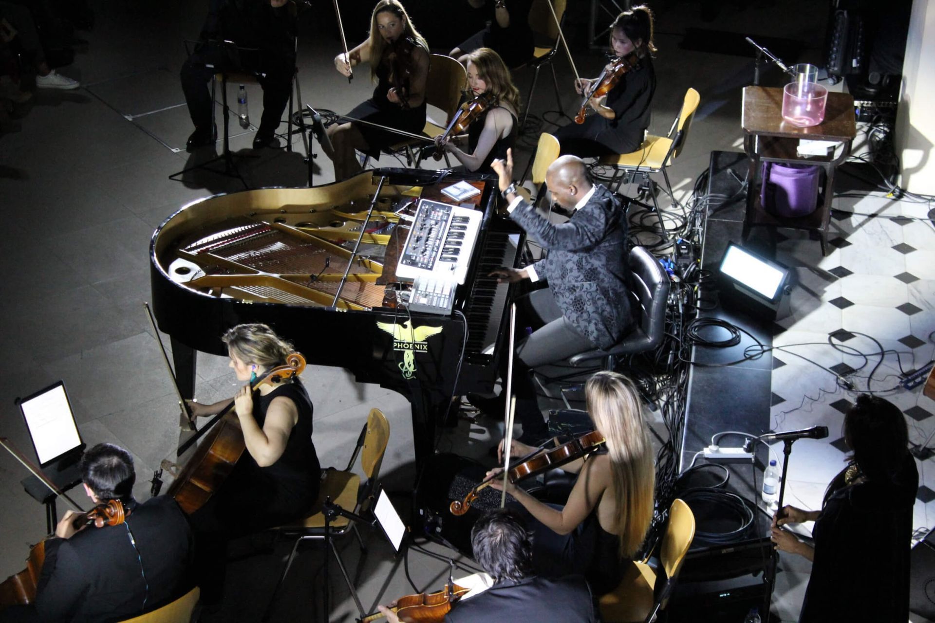 Orchestra performing with conductor and piano. Musicians playing instruments, stage lit.