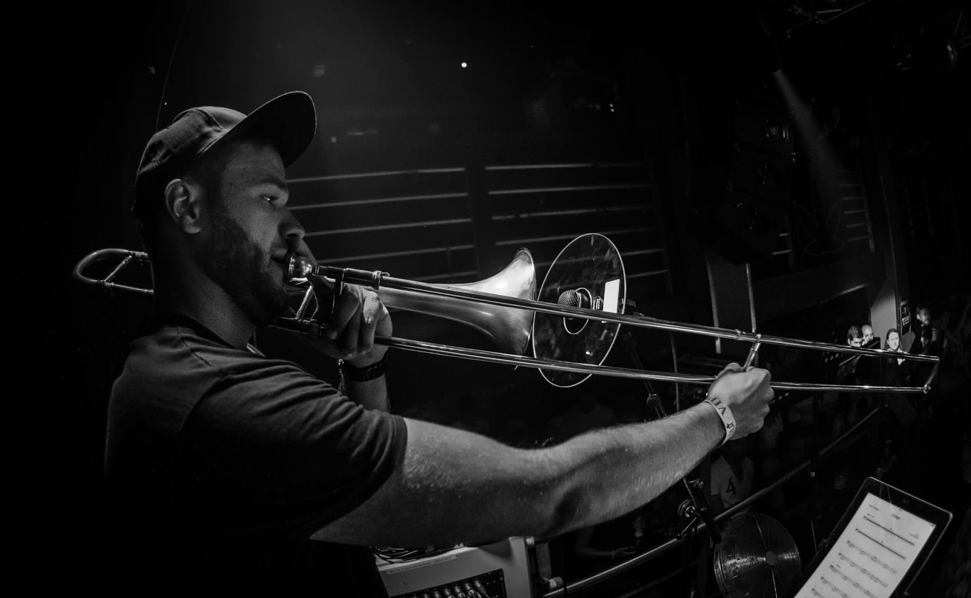 Man playing trombone onstage, illuminated in grayscale.