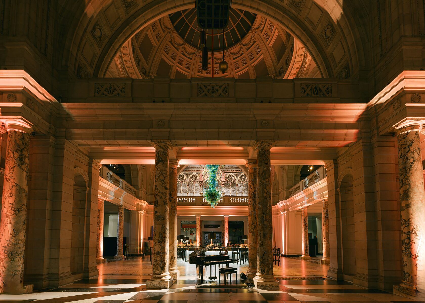 Grand hall with ornate columns, arched ceiling, and a grand piano. Illuminated in warm tones.