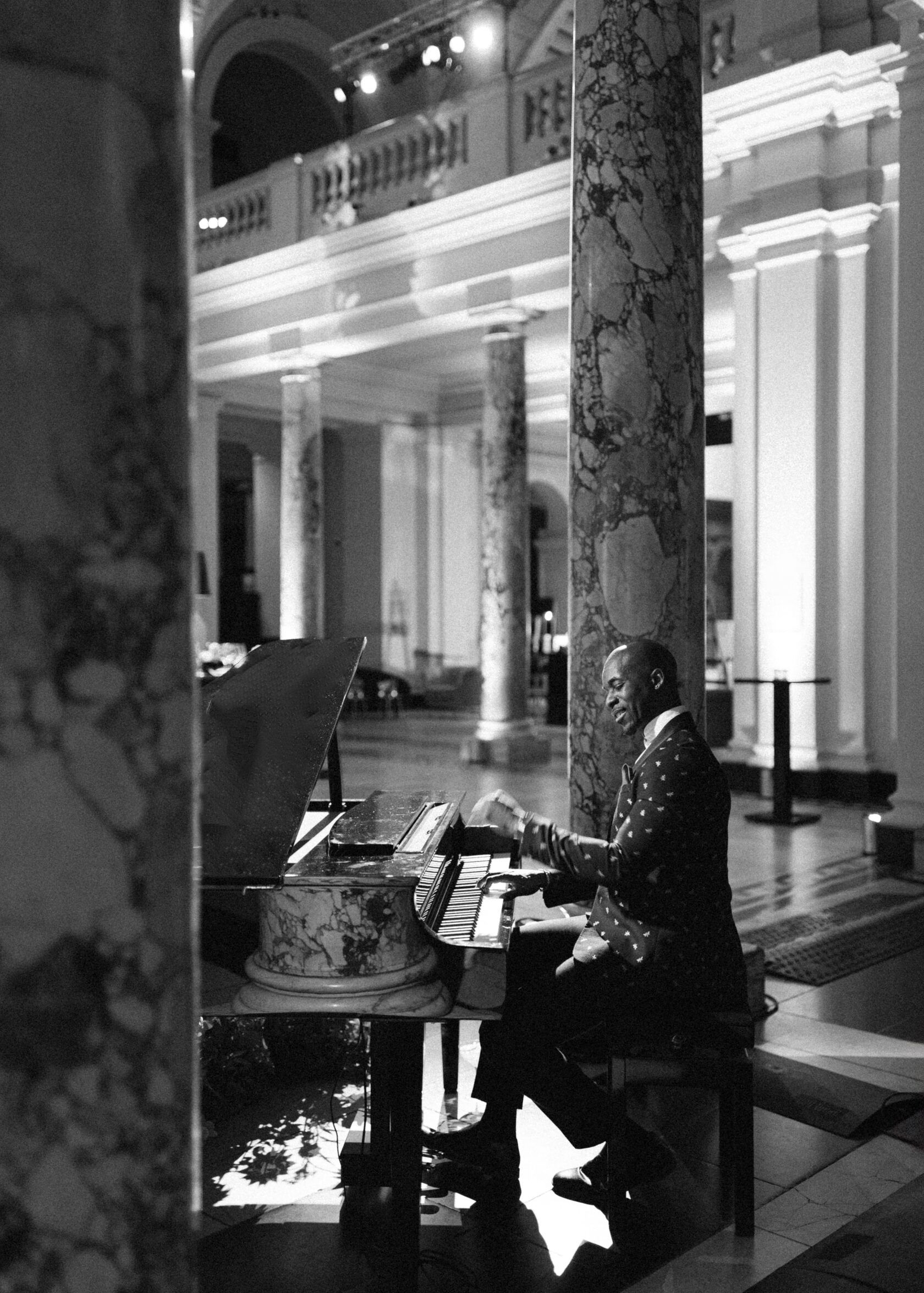 Man playing an organ in a grand hall with marble columns. Black and white.