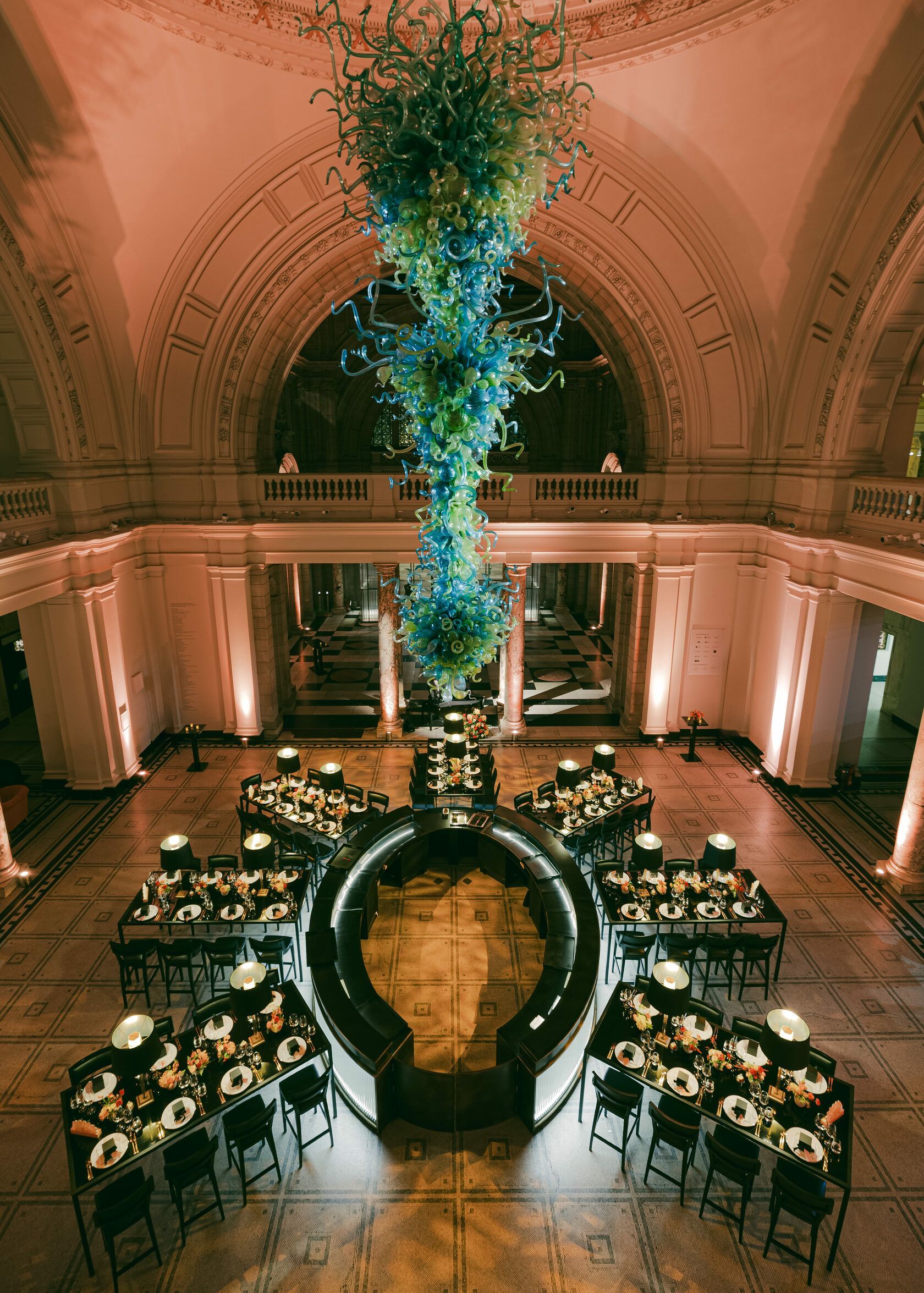 Grand dining hall with a large, colorful glass sculpture hanging above a circular table setting.