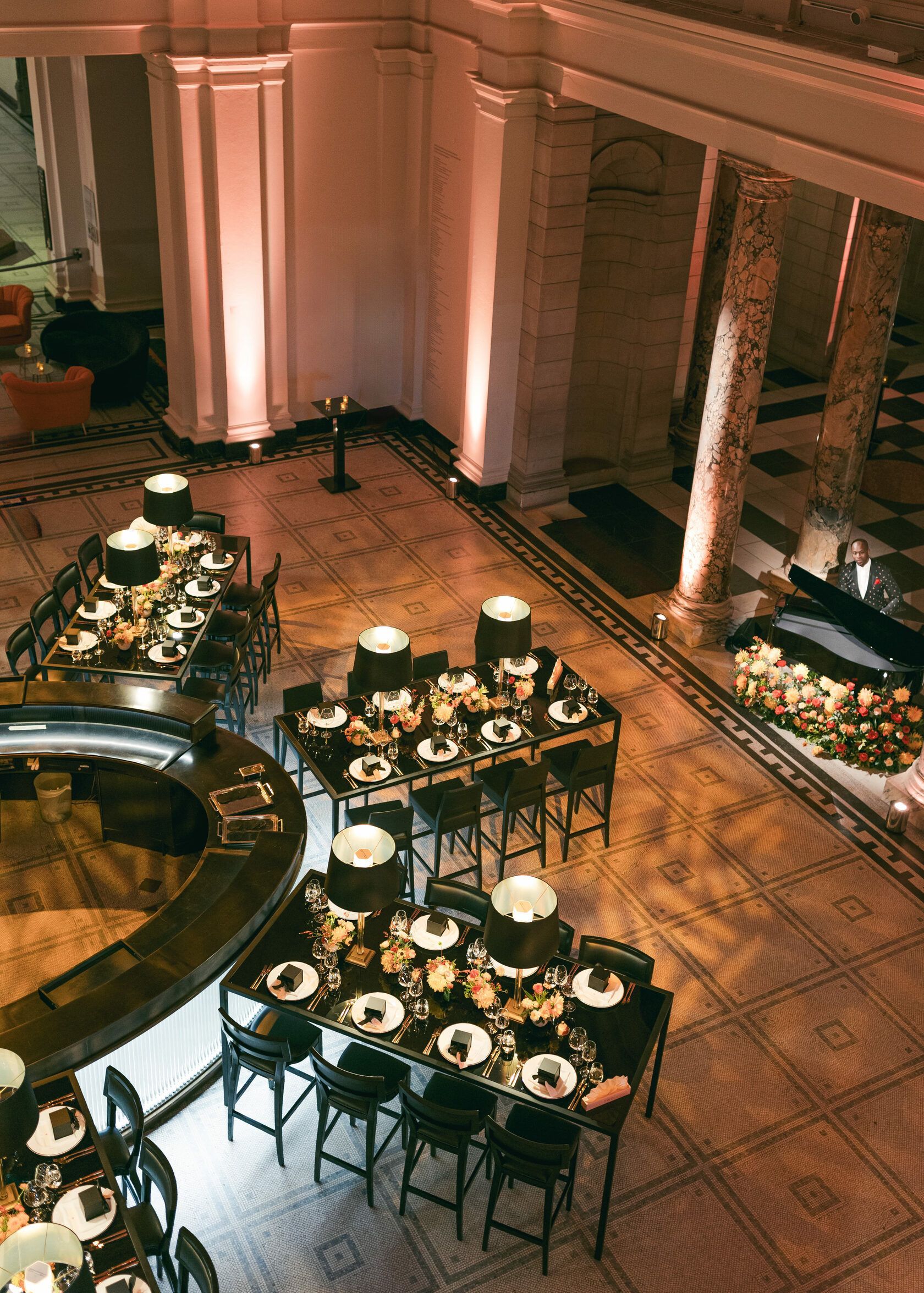High-angle view of a restaurant with multiple tables set for dining under warm lighting. Columns and mosaic floor.