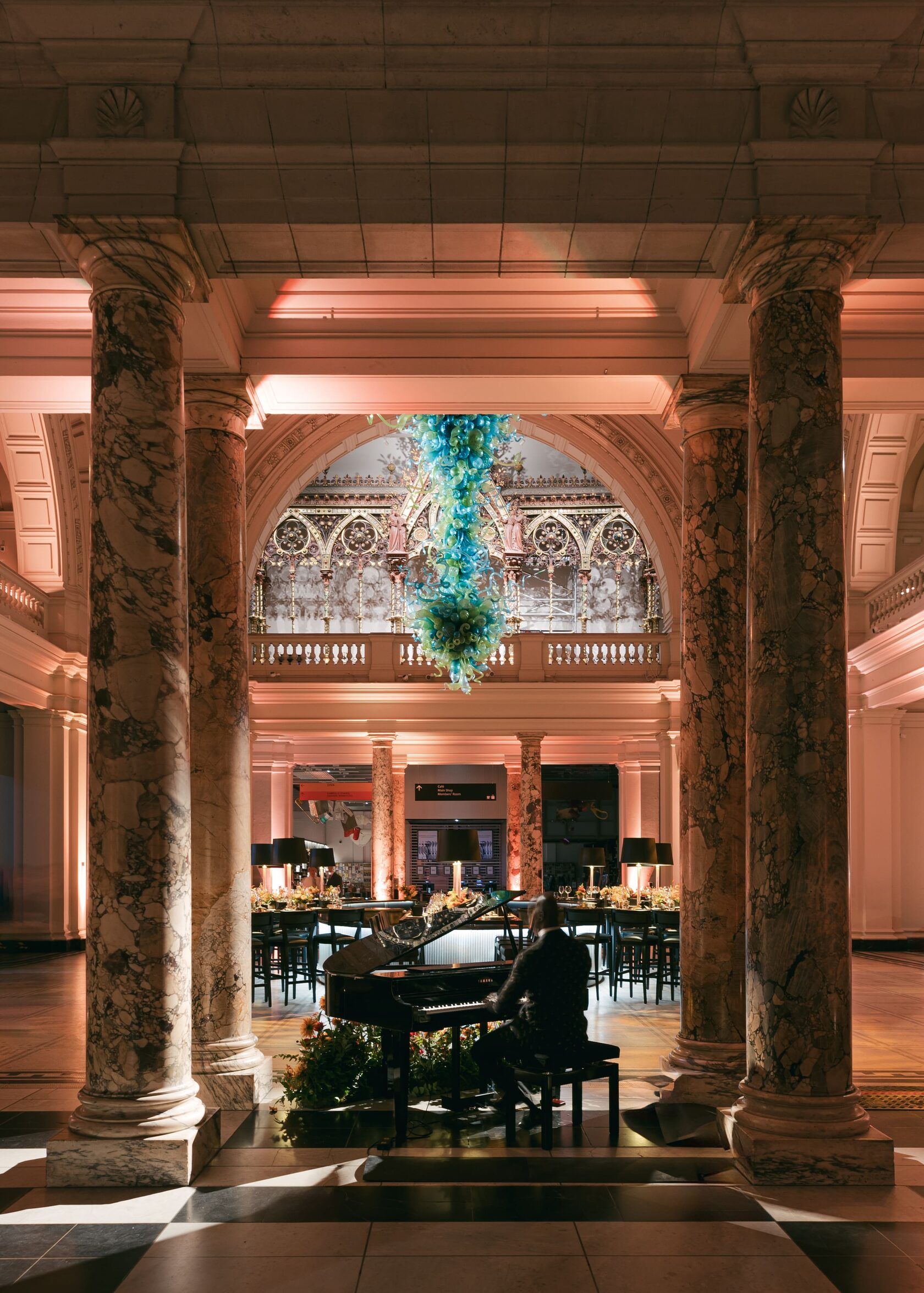 Ornate columns frame a room with a piano and tables. Soft lighting illuminates the space.