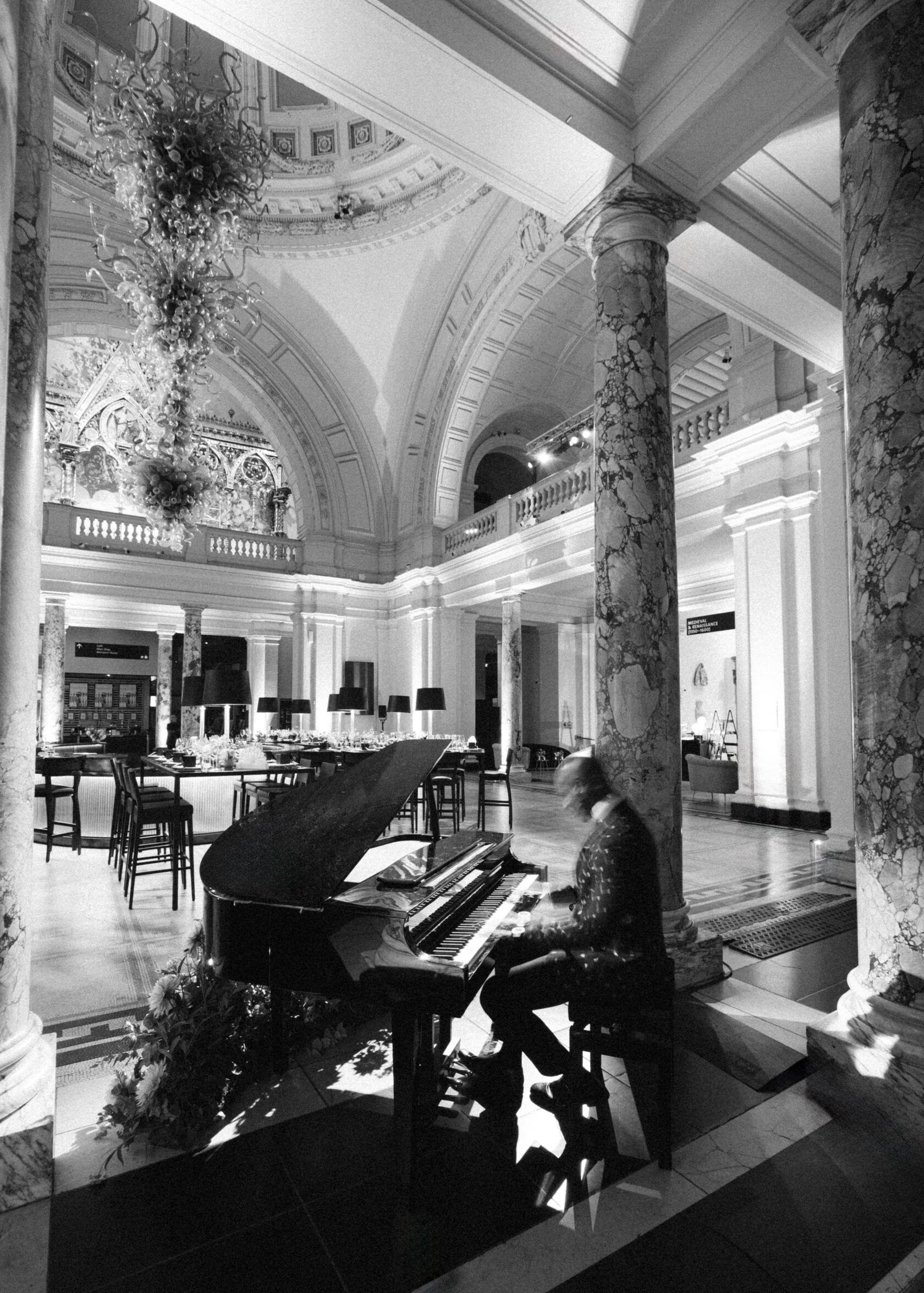 Pianist playing grand piano in a grand hall with ornate columns, high ceilings, and elaborate decorations.
