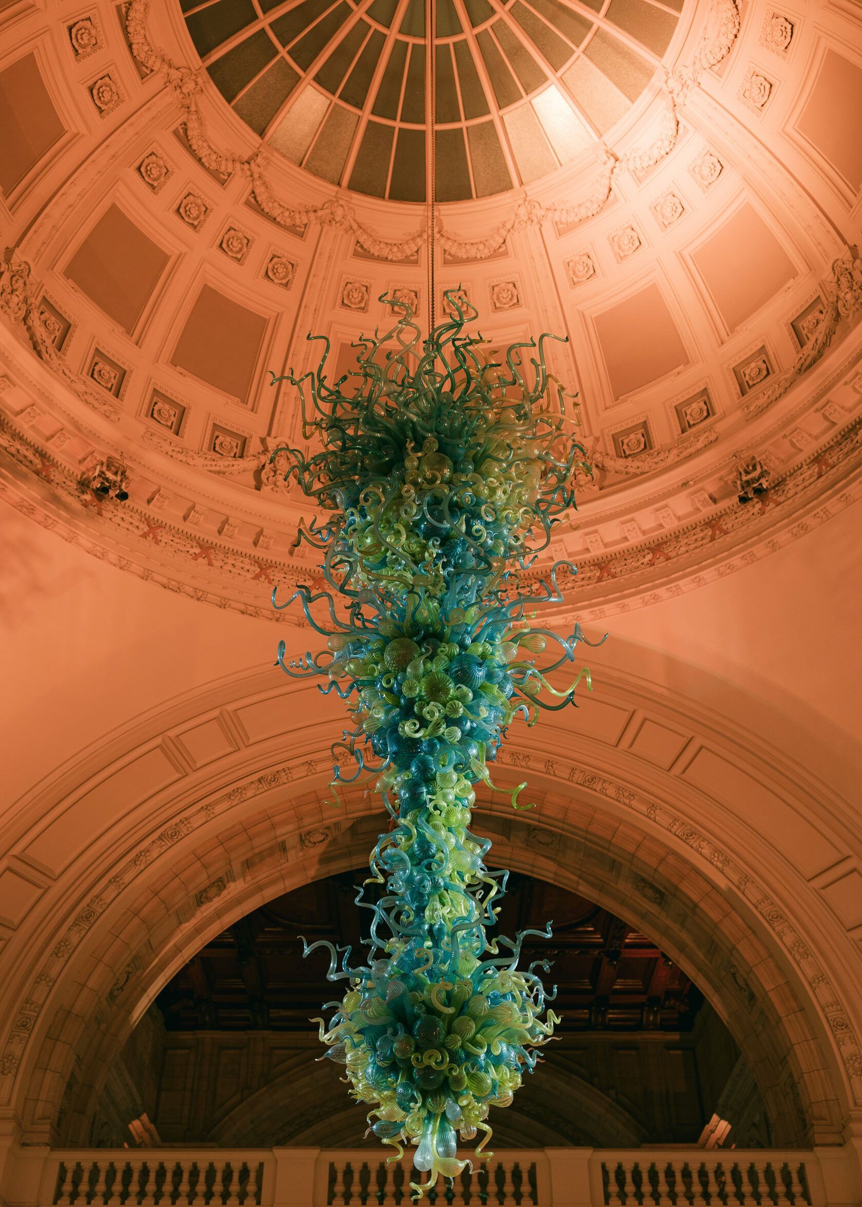 Large blue and green glass chandelier hangs from a domed ceiling.