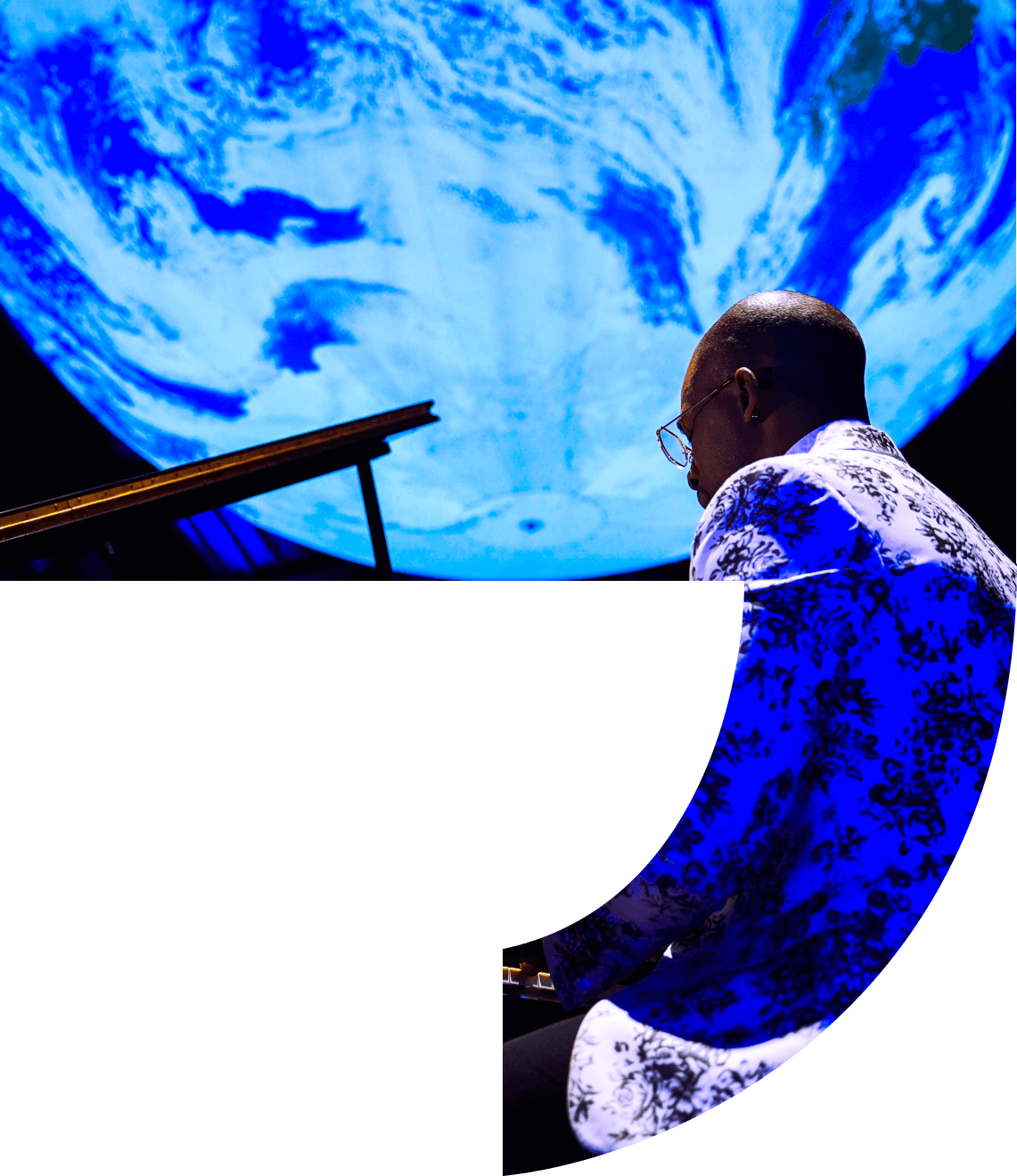 Pianist in floral shirt performs with Earth projected behind him; blue and white.