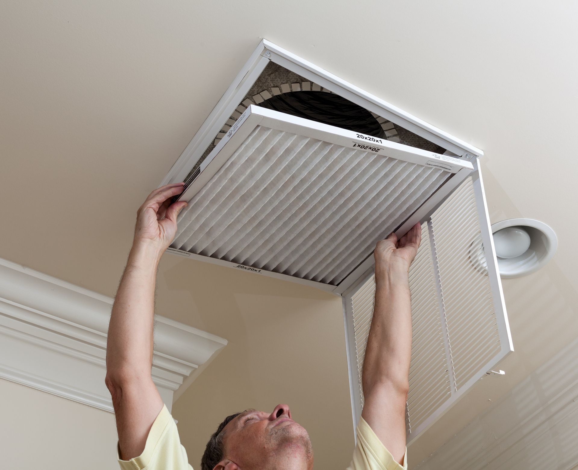Person replacing a white ceiling air filter in a home vent opening.