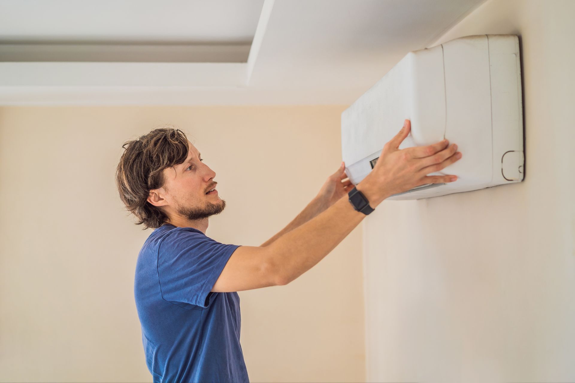 Airmax HVAC technician installing an air conditioning unit on a wall, indoor setting.