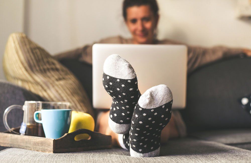 Woman relaxing on a couch with laptop, black polka dot socks, coffee, and fruit on a tray.