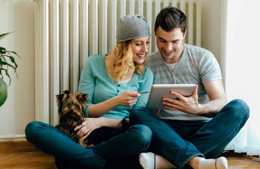 Couple smiling, shopping online with a tablet, dog sitting nearby.