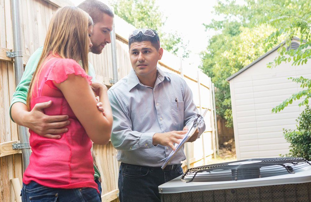 A couple reviews paperwork with an HVAC technician near an air conditioning unit outside.
