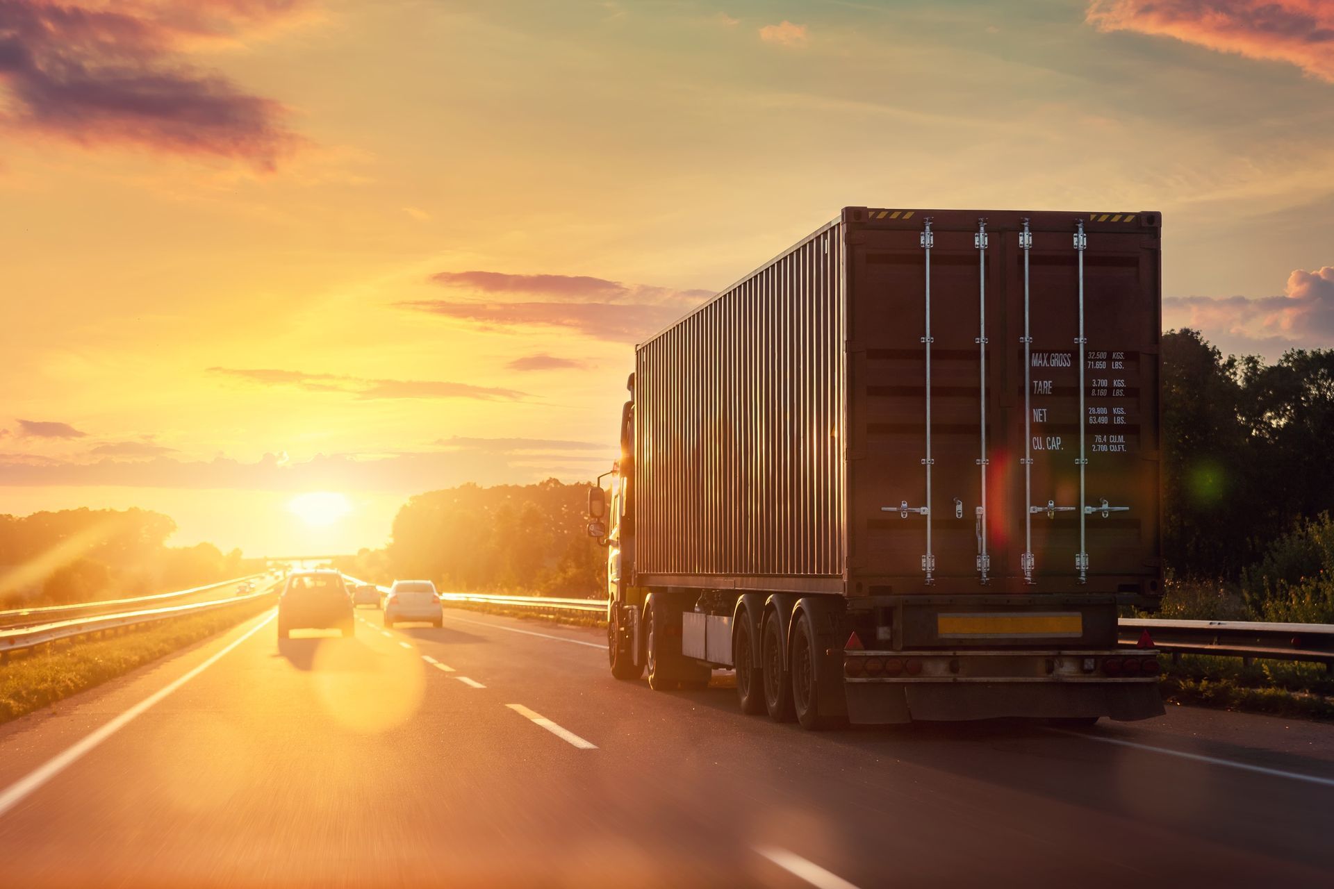 A semi truck is driving down a highway at sunset.