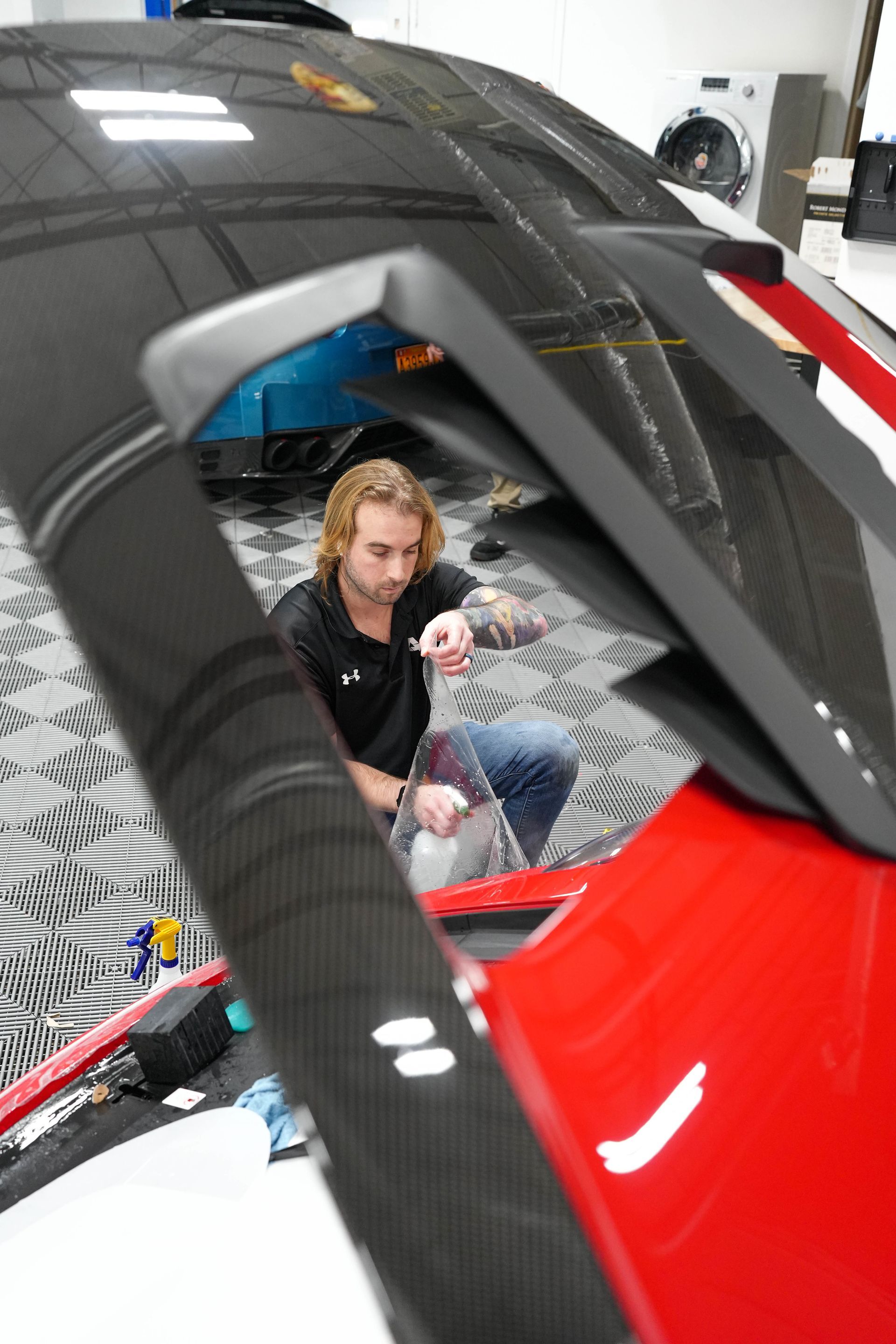 Man working on a car, with focus on the wing. He is holding a tool, in a garage setting.