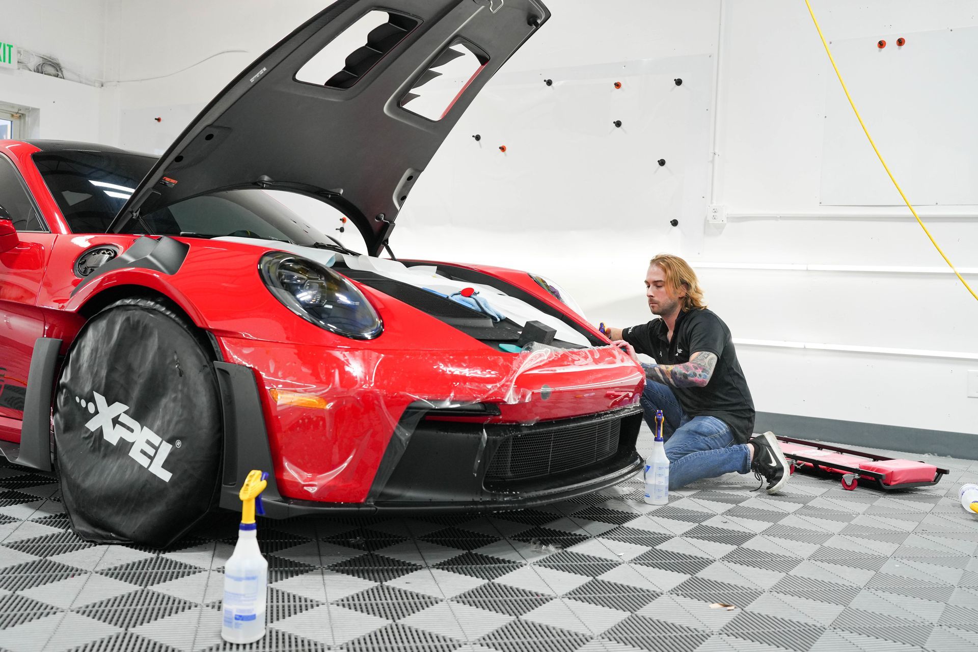 A mechanic working on a red Porsche in a garage, applying protective film.