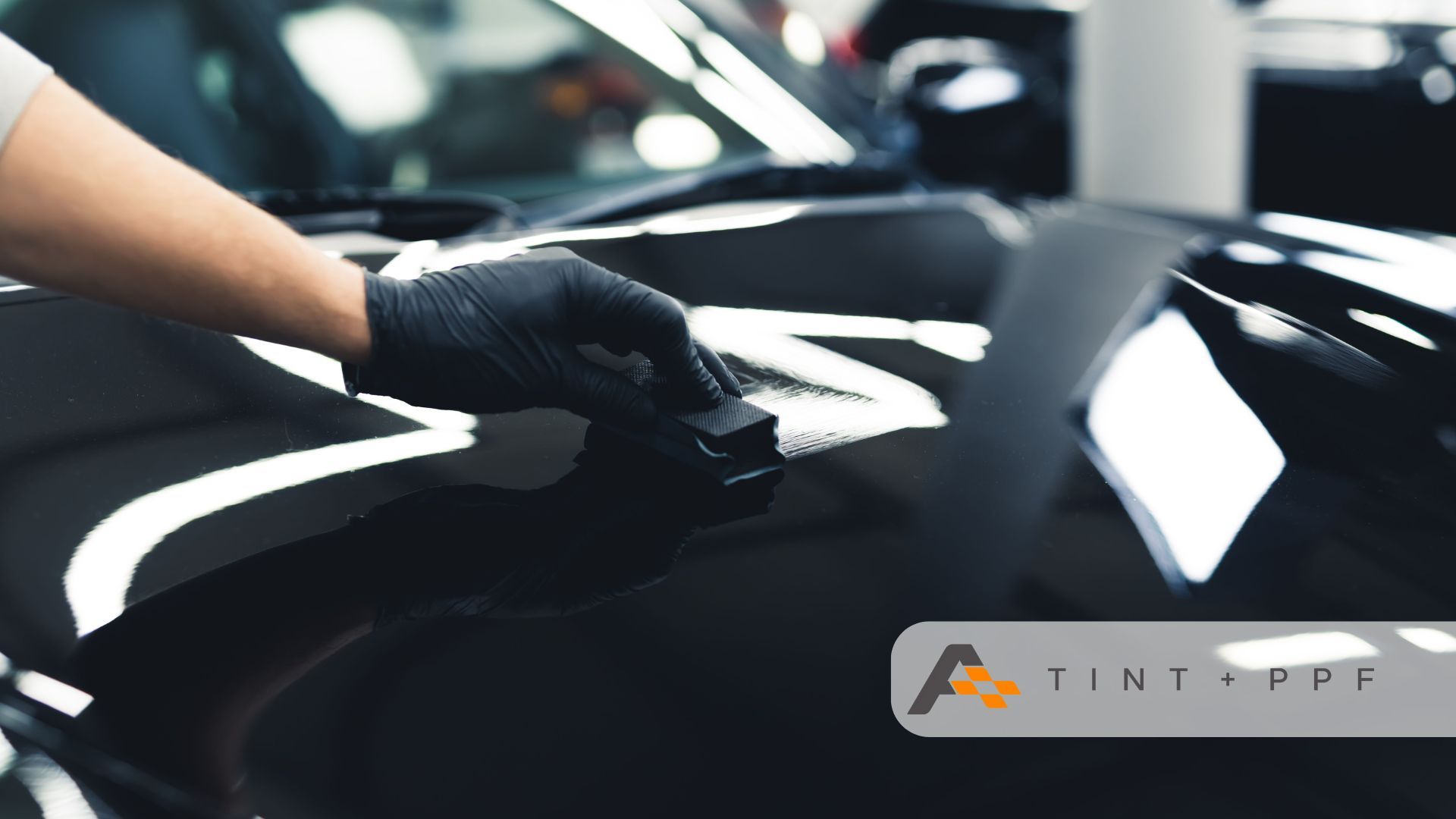 A person applying ceramic coating to a black car's surface using a microfiber applicator pad