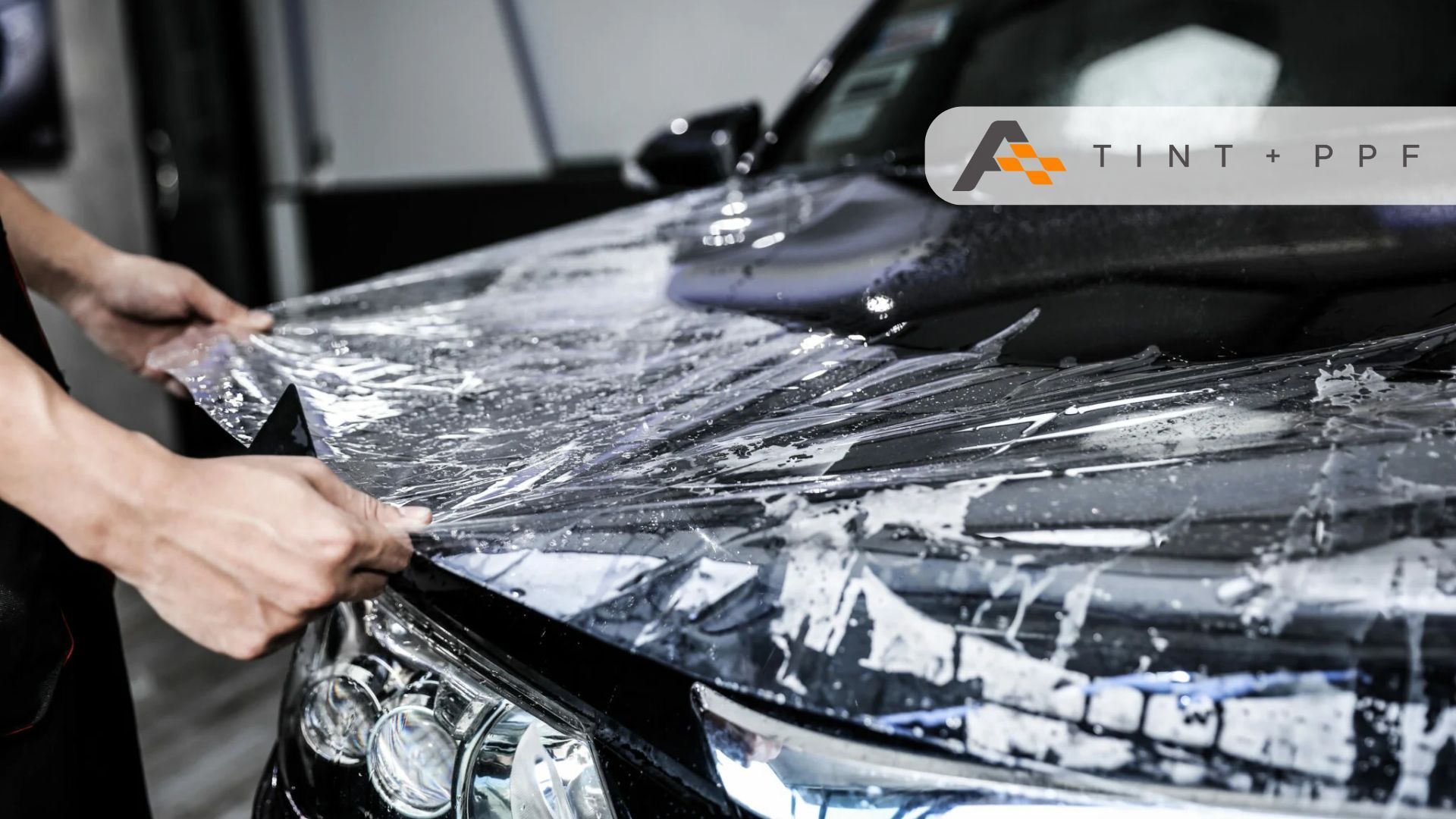 A technician applies paint protection film to a wet black car hood