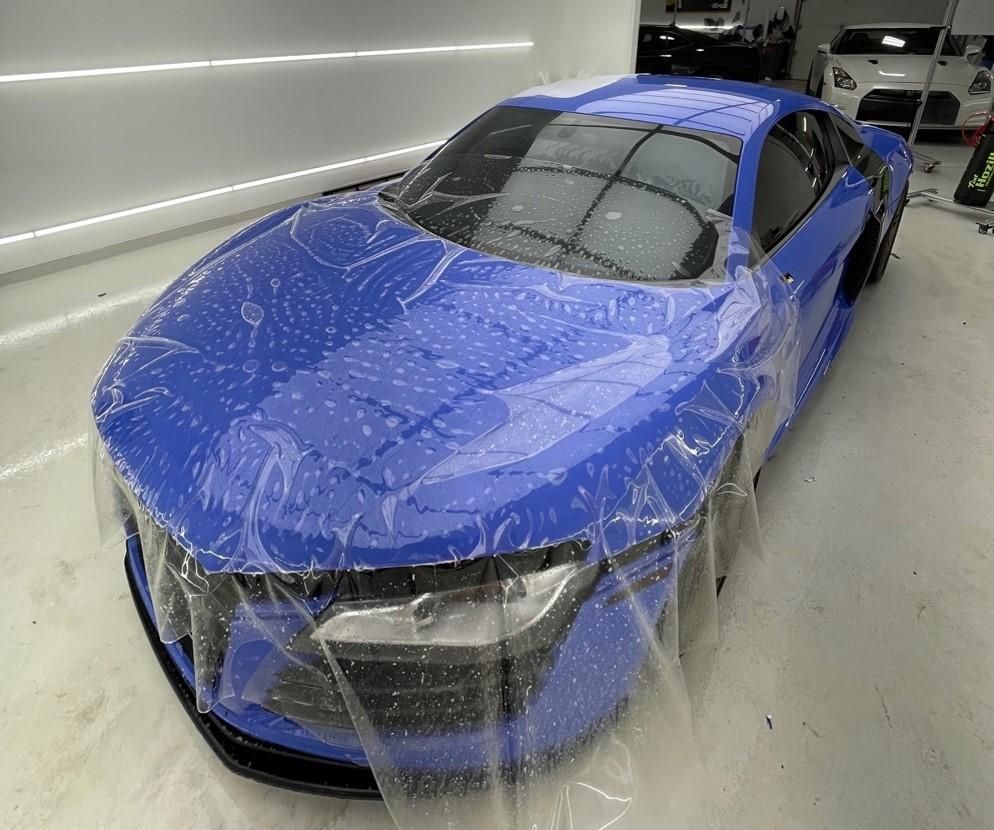A blue sports car is wrapped in plastic in a garage.