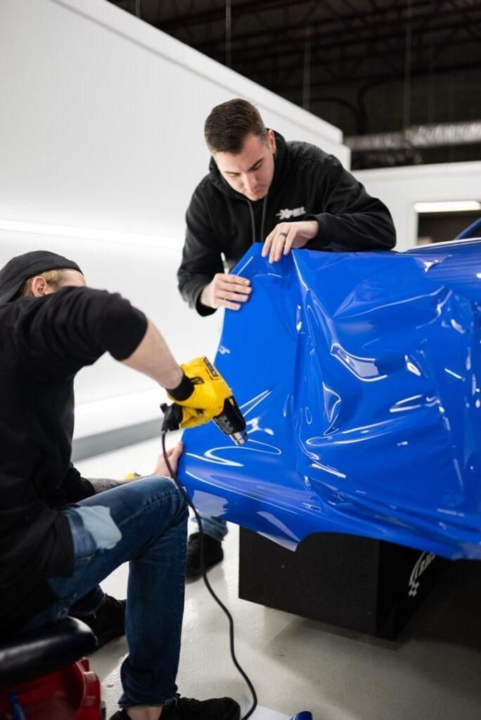 Two men are wrapping a blue car with vinyl.