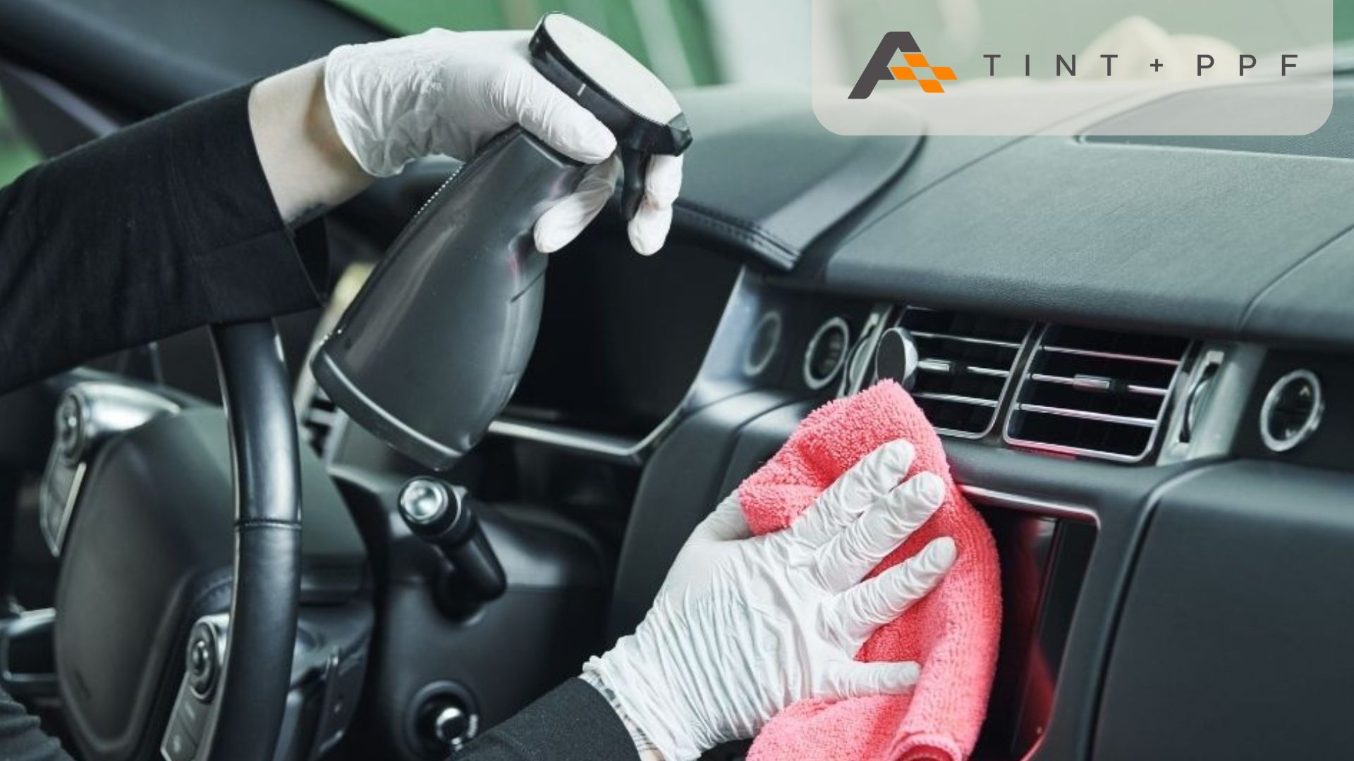 A gloved professional sprays and wipes down a car's interior console with a microfiber cloth.