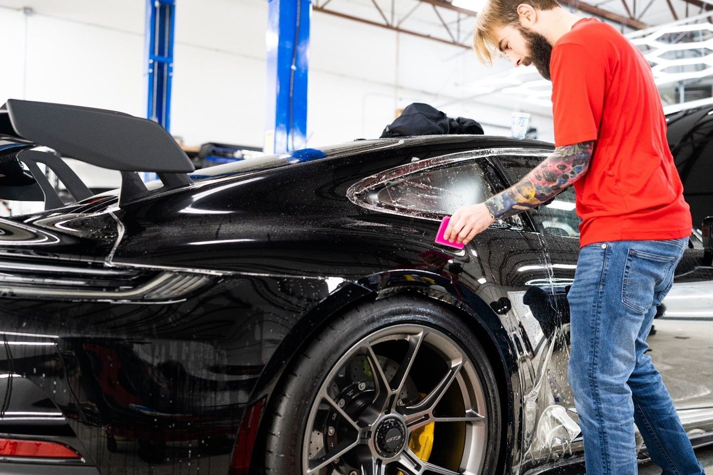 A man is wrapping a black sports car with a purple cloth.