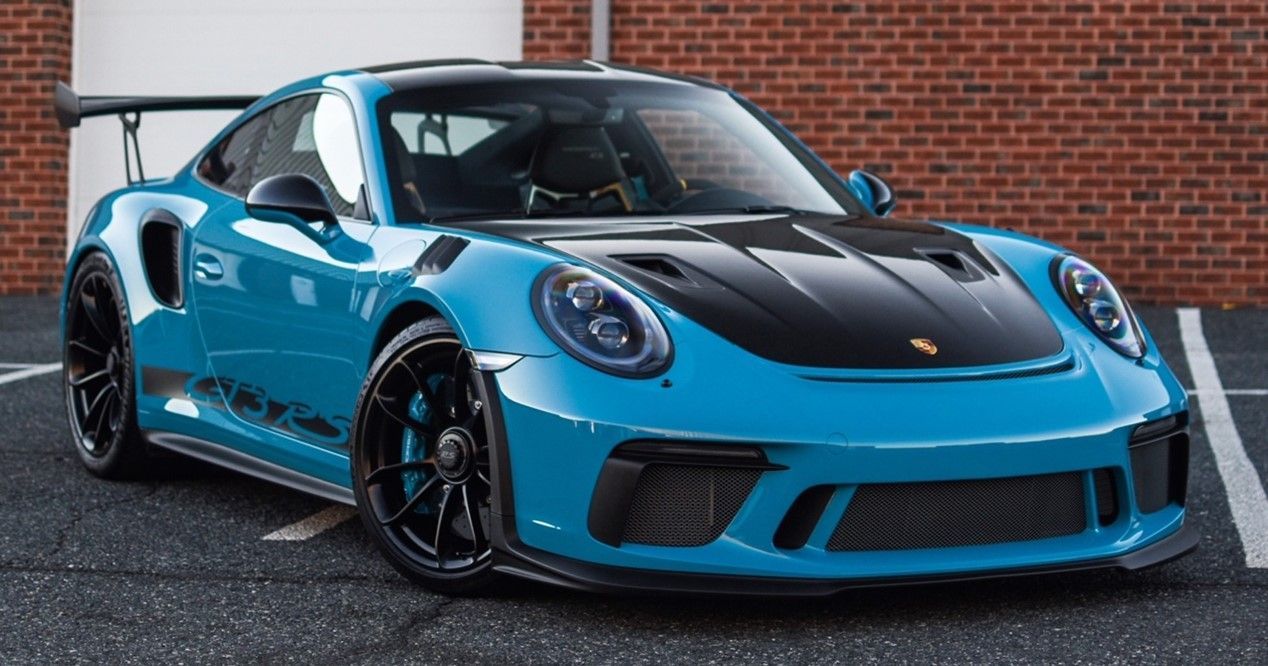 A blue porsche 911 gt3 rs is parked in a parking lot in front of a brick building.