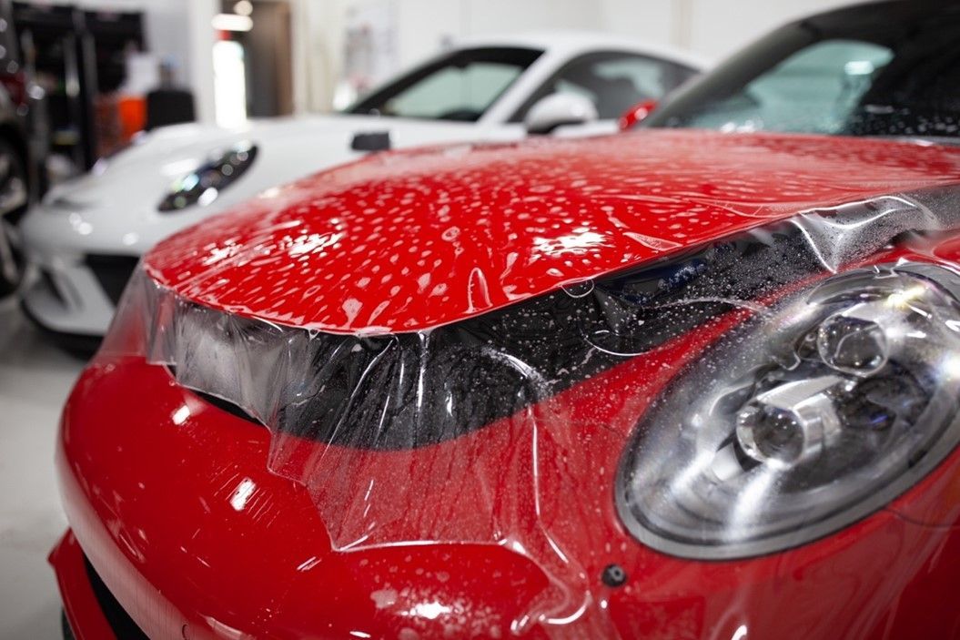 A close up of a red car with a protective film on the hood.