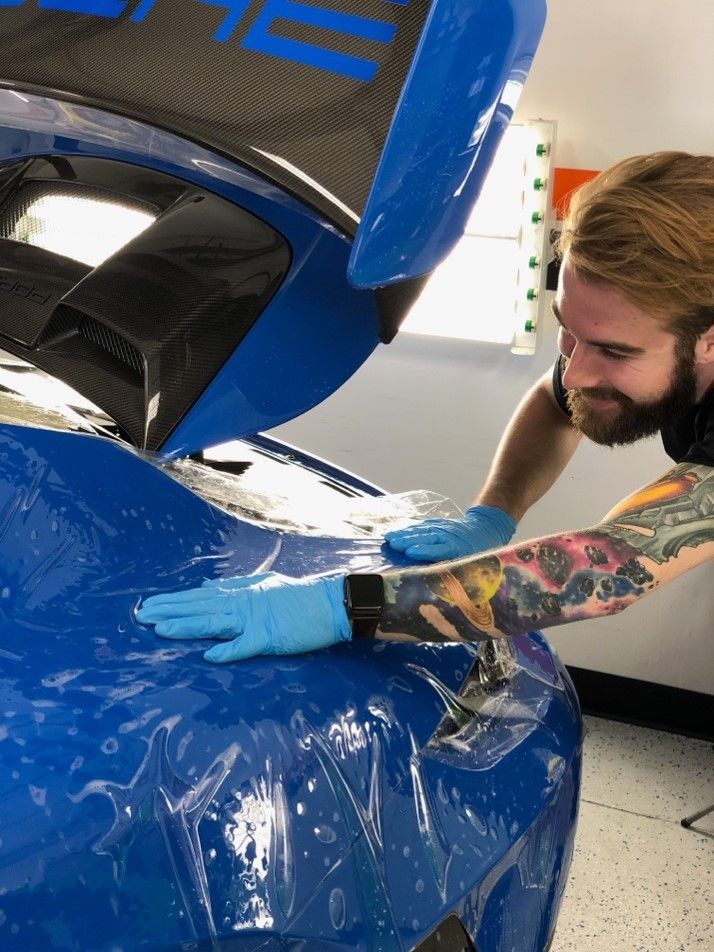 A man is wrapping a blue car with plastic wrap.