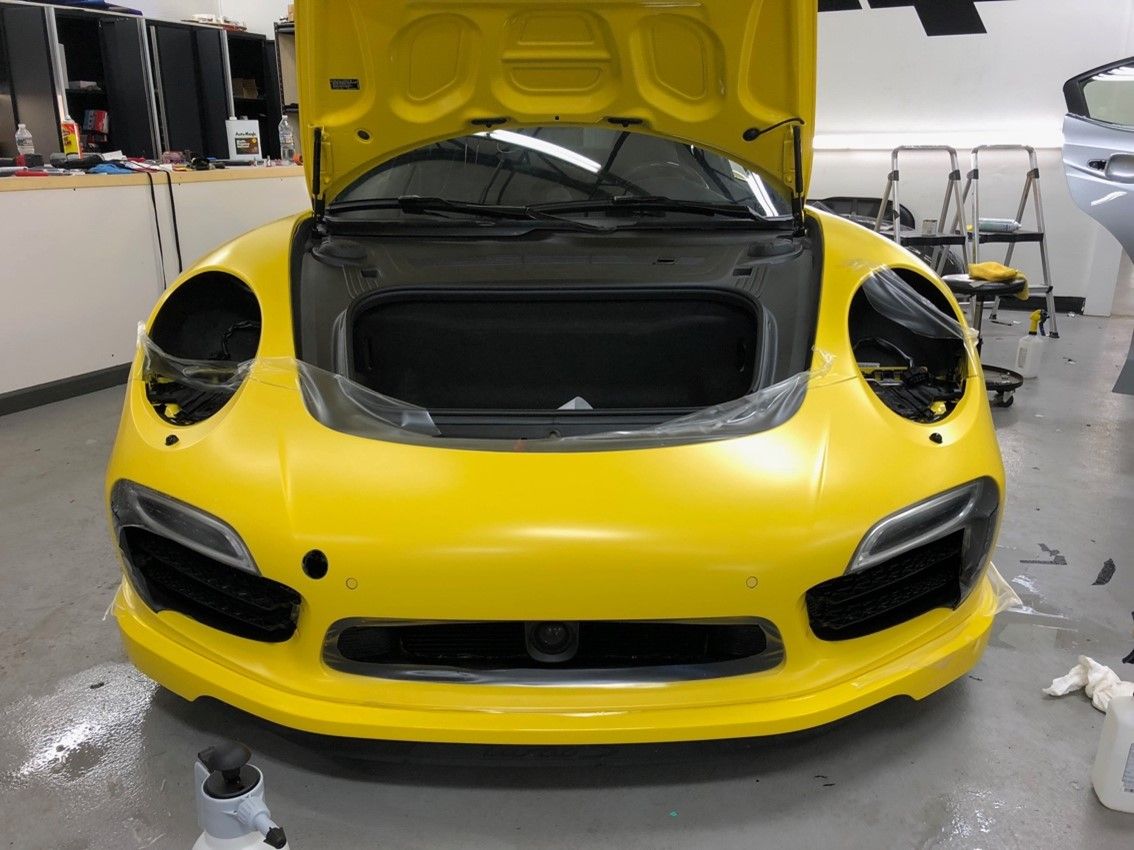 A yellow sports car with the hood up in a garage.