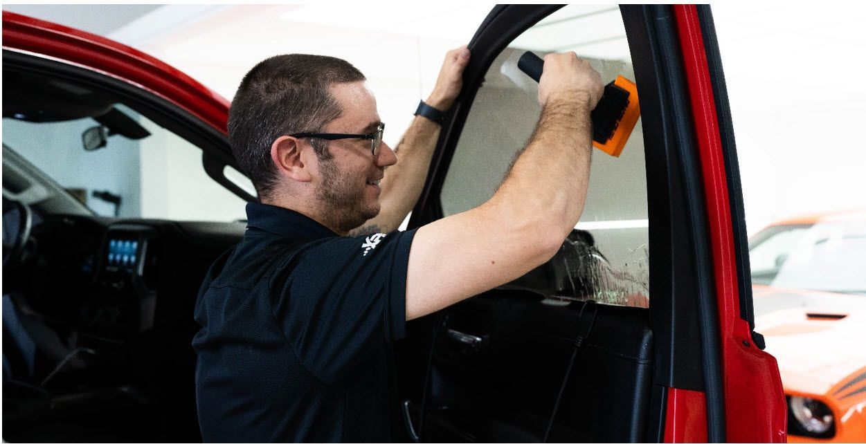 A man is installing window tinting on a red car.