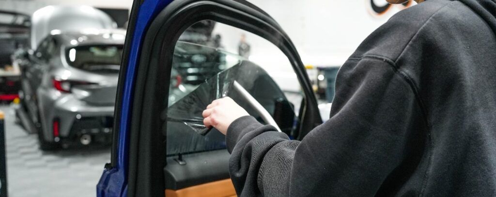 A person is applying tinted glass to a car window.