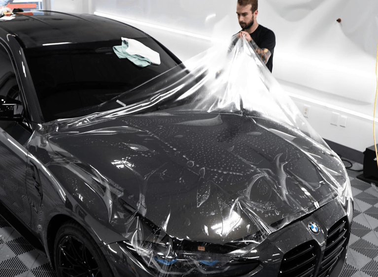 A man is wrapping a car with clear plastic.